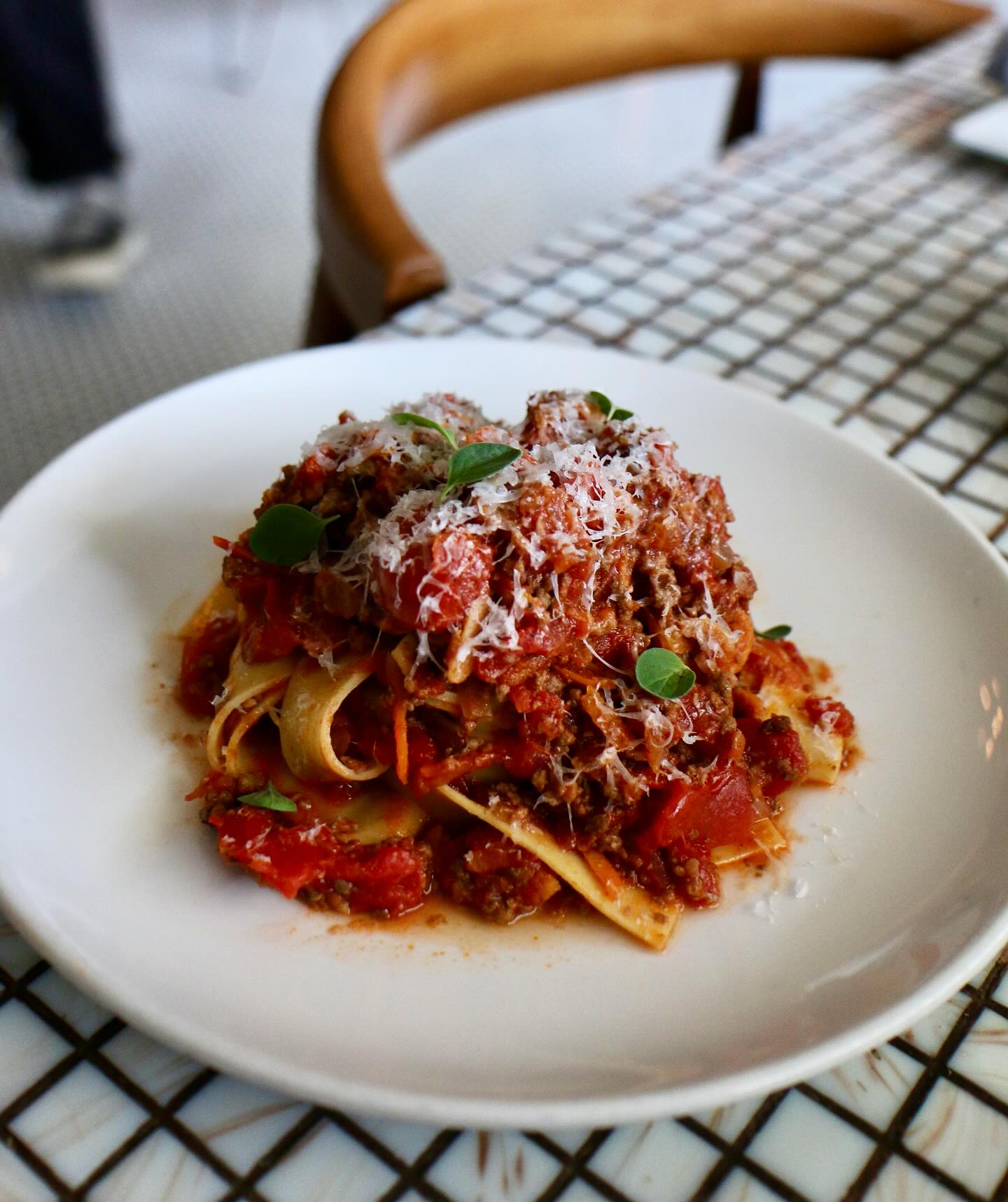 Pappardelle pasta with meat sauce, grated cheese, and green herbs.