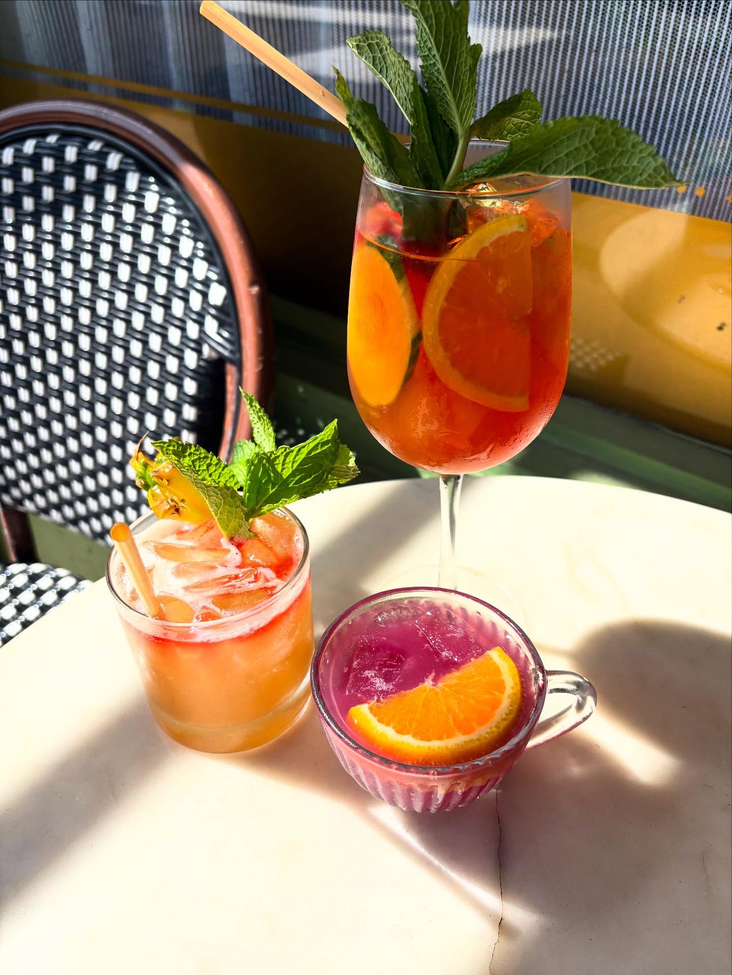 Three varied drinks with fruit and mint on a sunlit table.