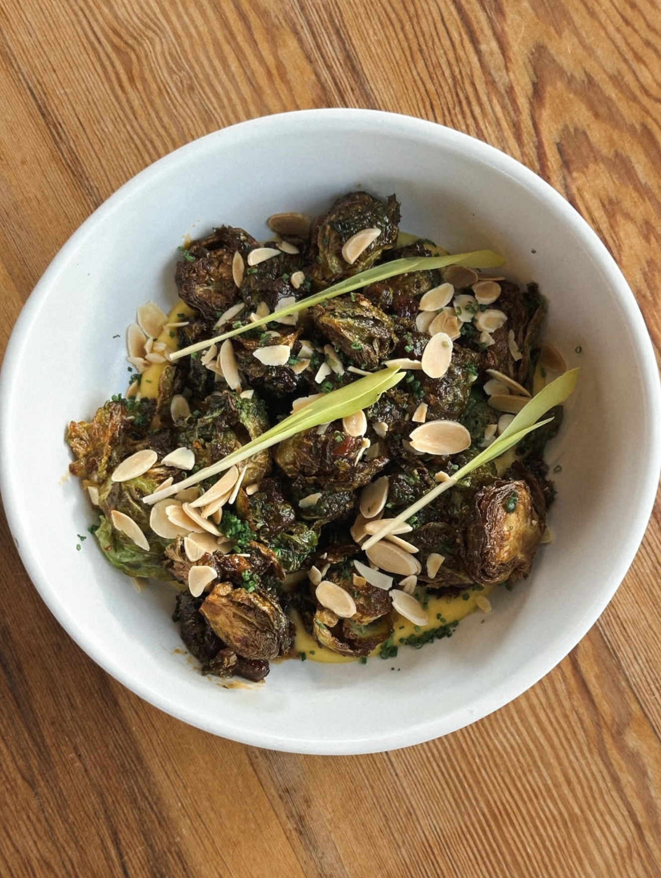 Roasted Brussels sprouts with almonds, green garnish, and creamy sauce.