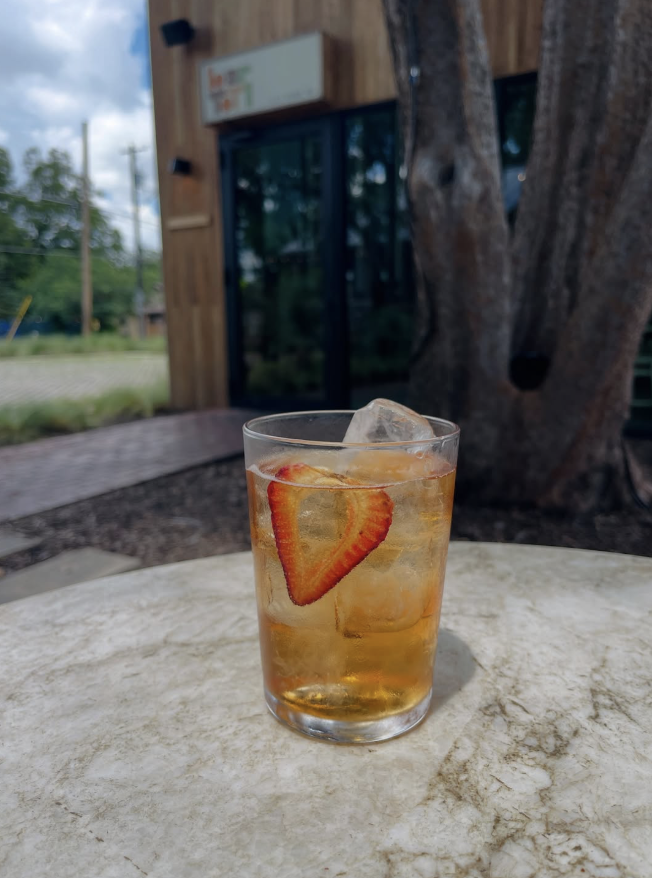A glass of iced drink with a strawberry slice on an outdoor table.