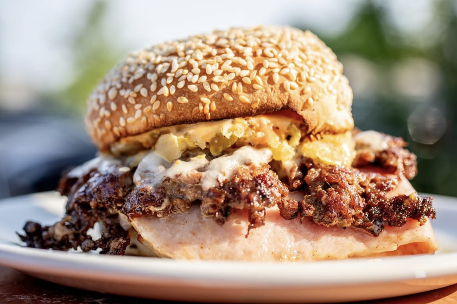A thick sandwich with a sesame bun, crispy topping, and melted sauce.
