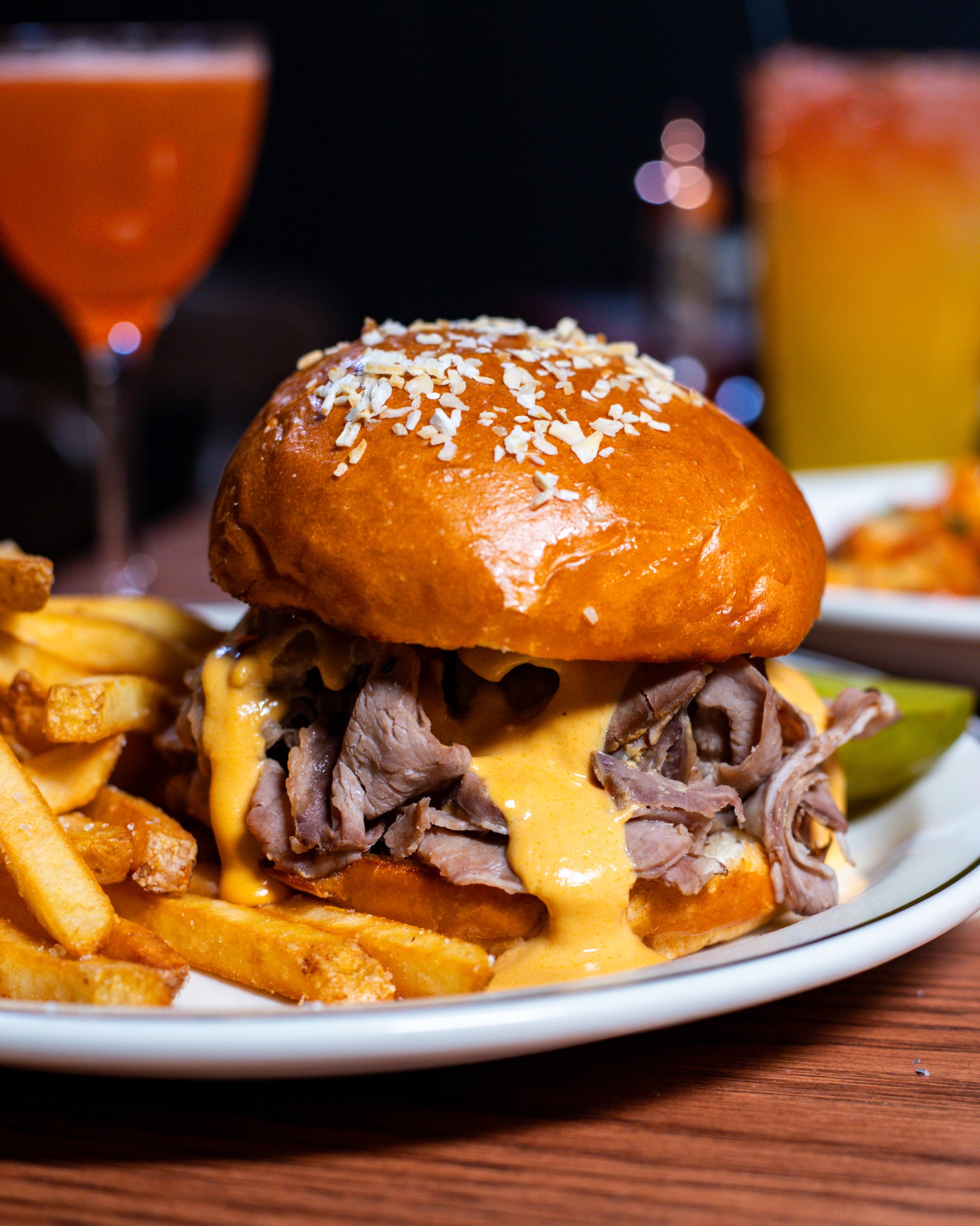 Sandwich with sliced meat, orange sauce, fries, and a pickle.