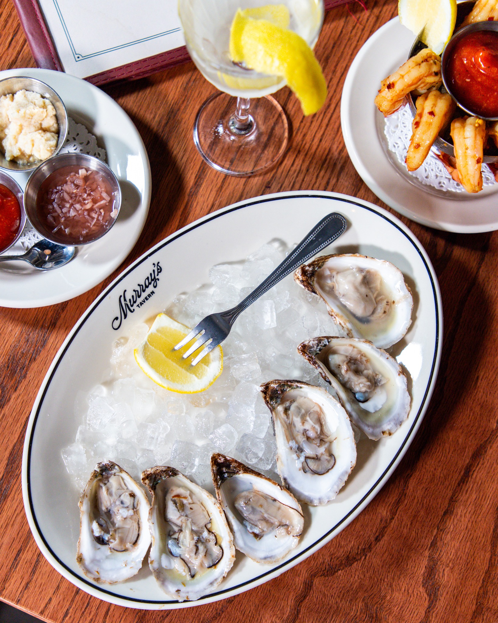 Raw oysters on ice, lemon, sauces, shrimp, and a cocktail.