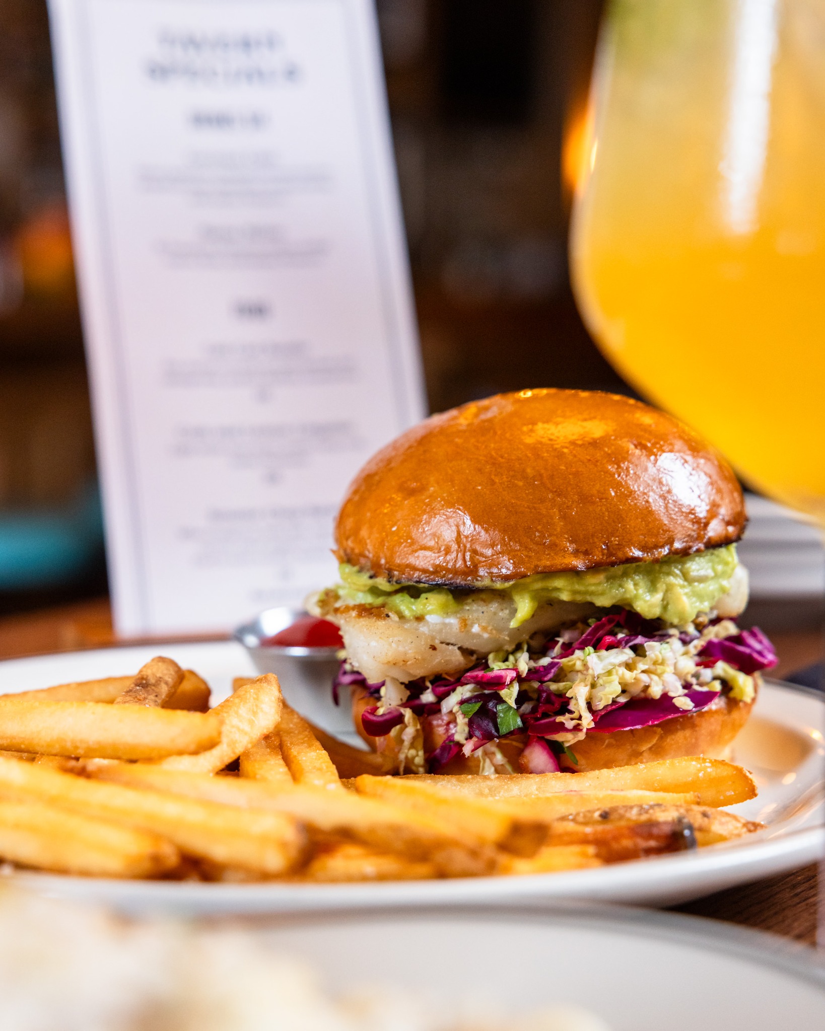 Seafood burger with fries, guacamole, coleslaw, and ketchup on a plate.