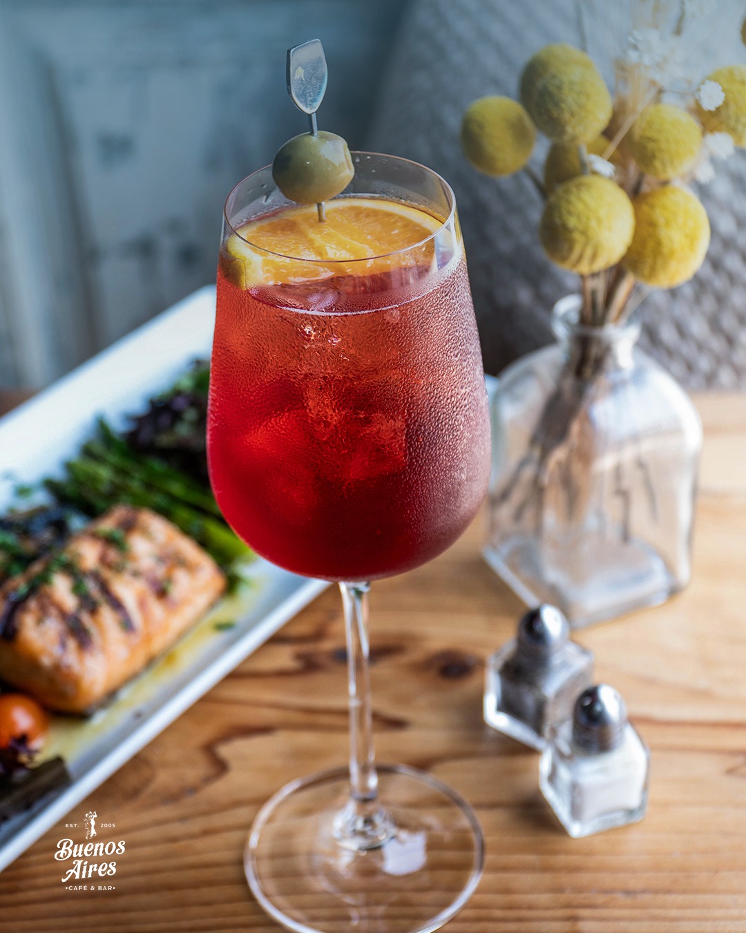 Chilled red cocktail with orange, olive, and a salmon meal.