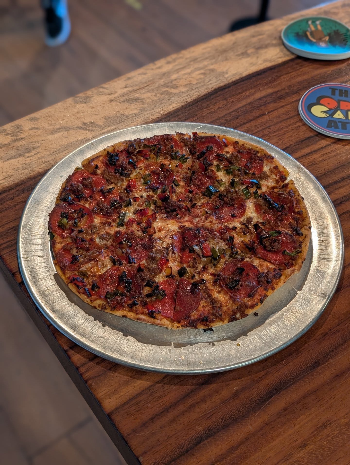Whole pizza with pepperoni, sausage, and green peppers on a metal pan.