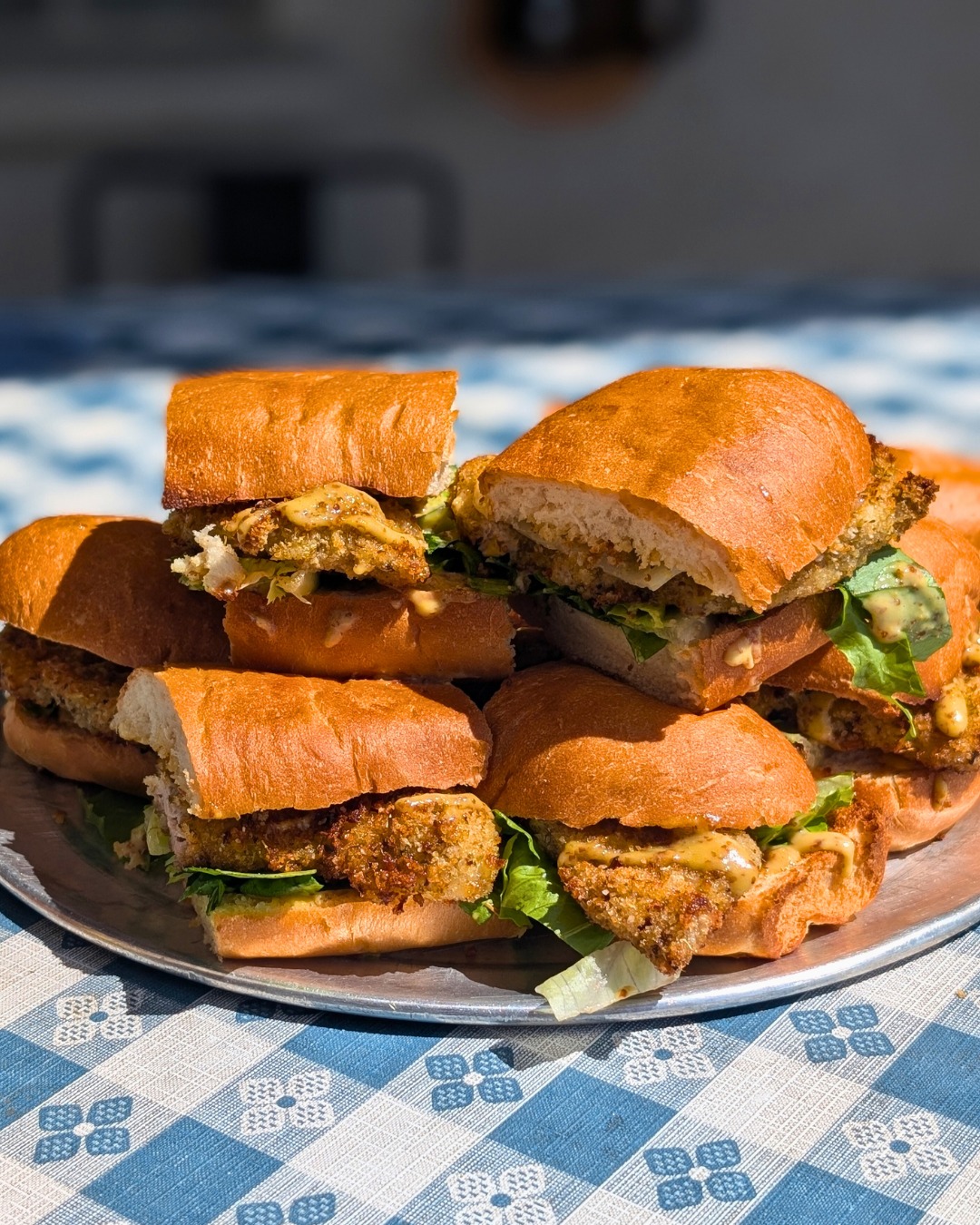 Stack of fried sandwiches with lettuce and sauce on a metal tray.