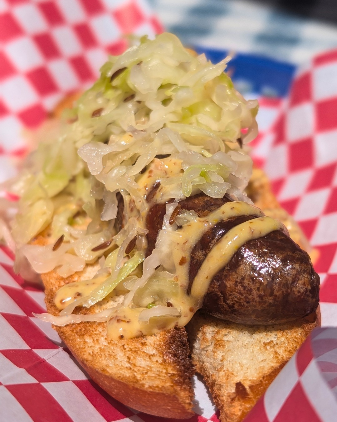 Sausage in a bun with sauerkraut and mustard on checkered paper.