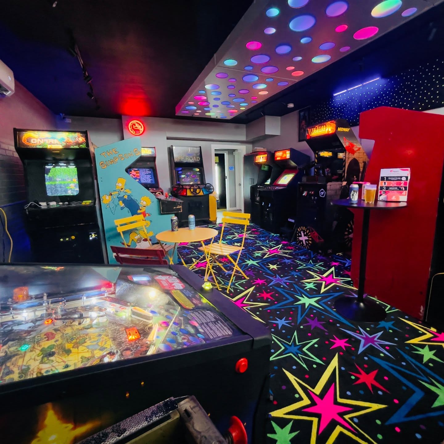 Pinball machine and video game arcade with colorful lights and star carpet.