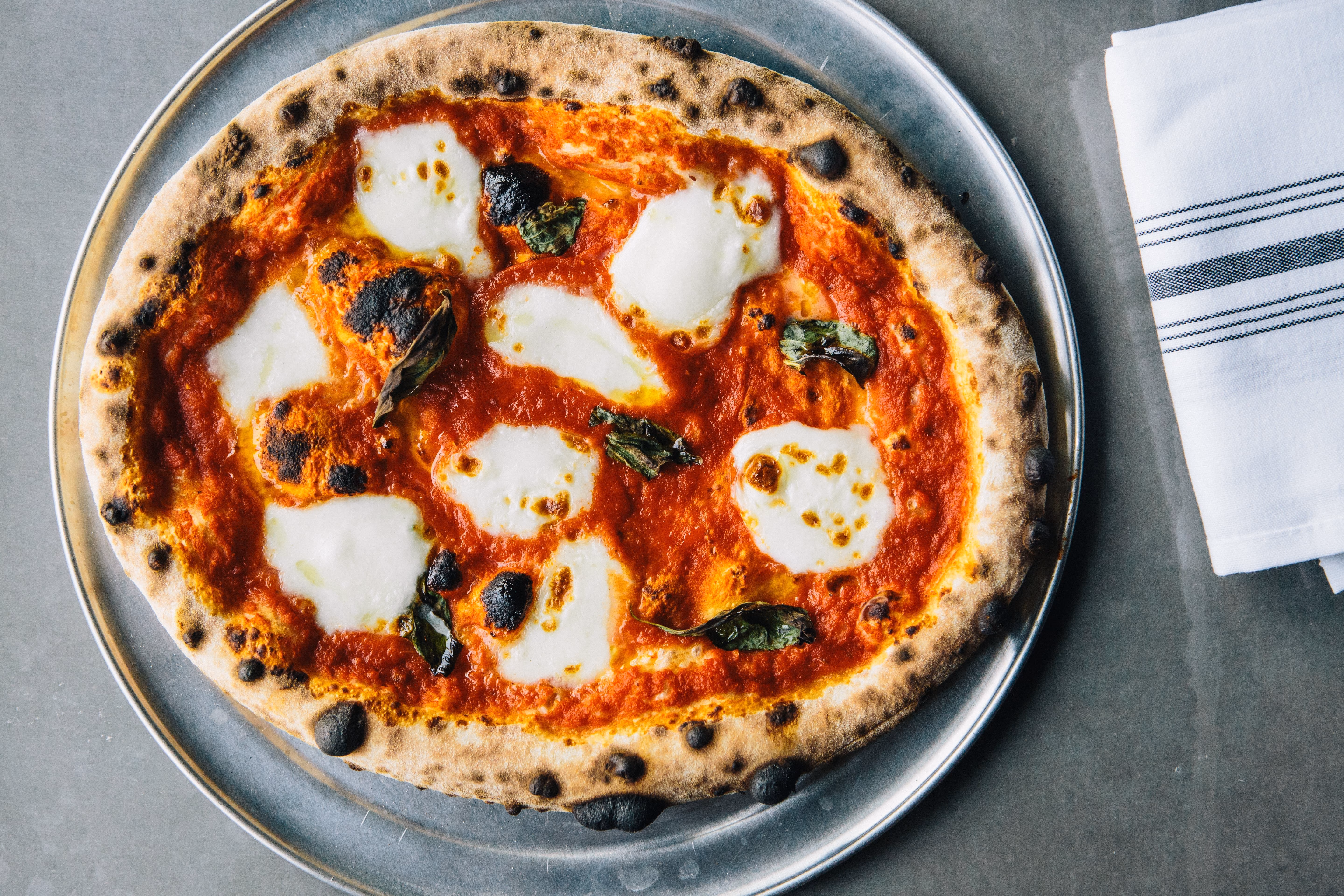 Margherita pizza with mozzarella and basil on a metal tray.