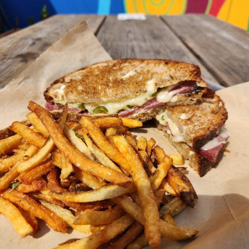 A corned beef sandwich with melted cheese and fries on a wooden table.