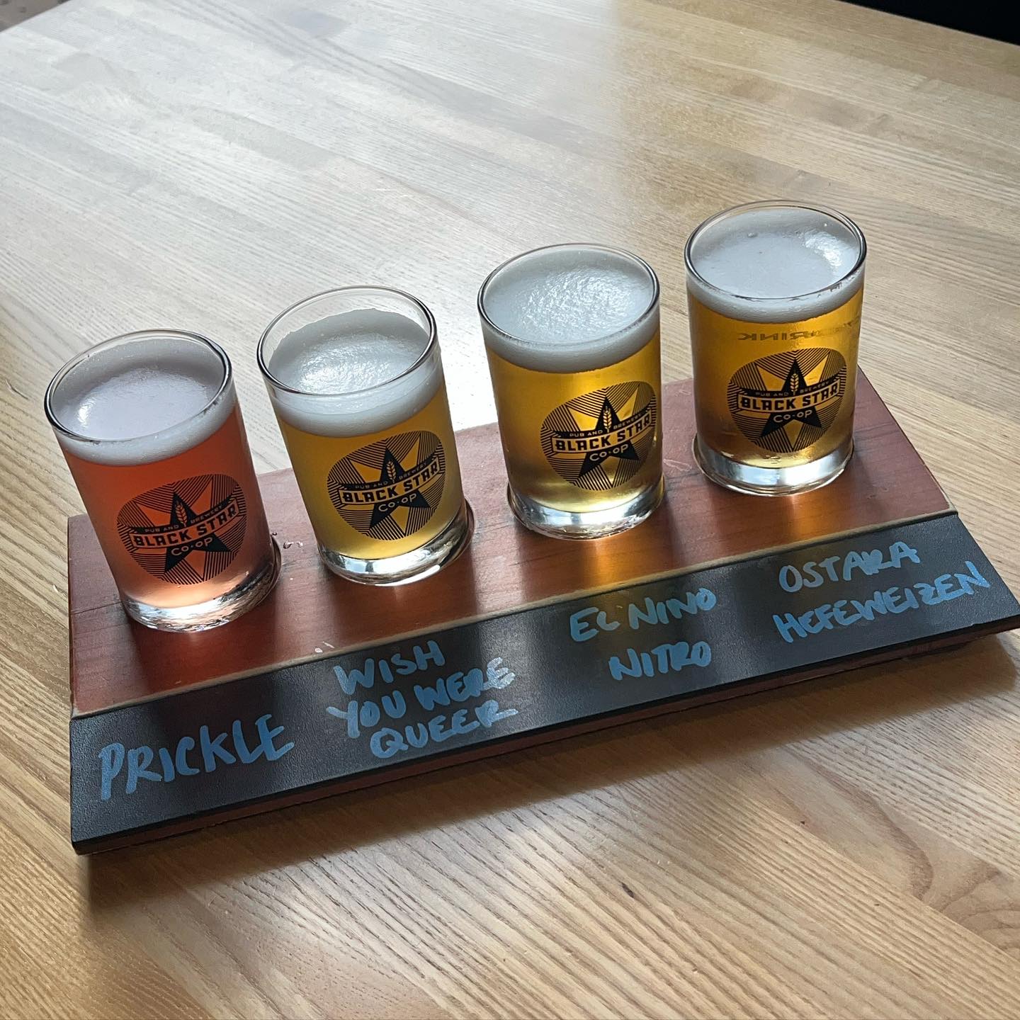 Four different Black Star Co-op beers on a wooden flight.