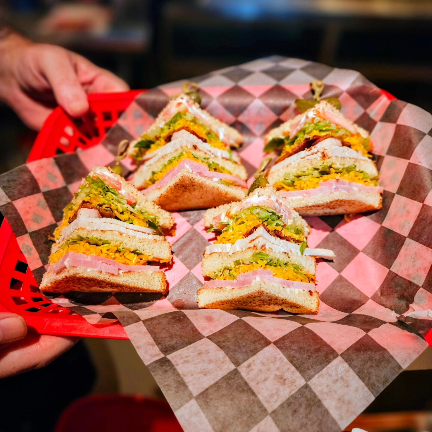 Multiple triangular club sandwiches with pickles in a red basket.