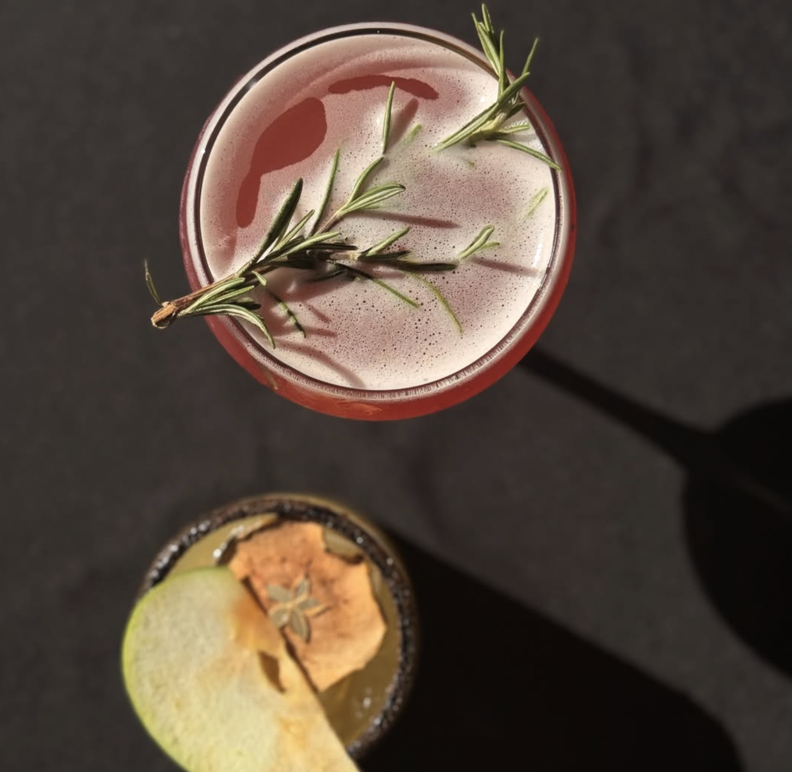 Two cocktails from above, garnished with rosemary and an apple slice.