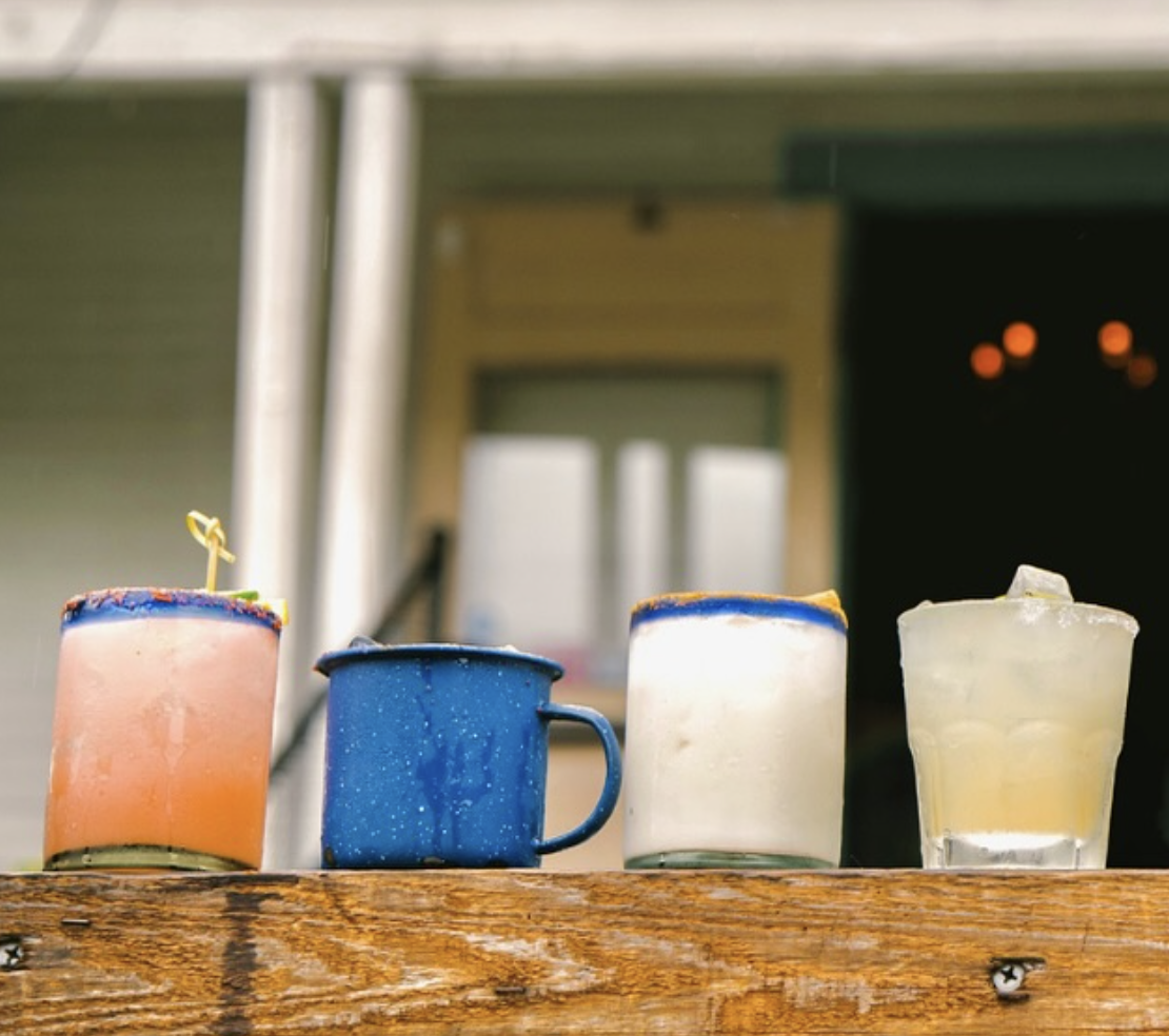 Four different drinks and a blue mug on a wooden surface.