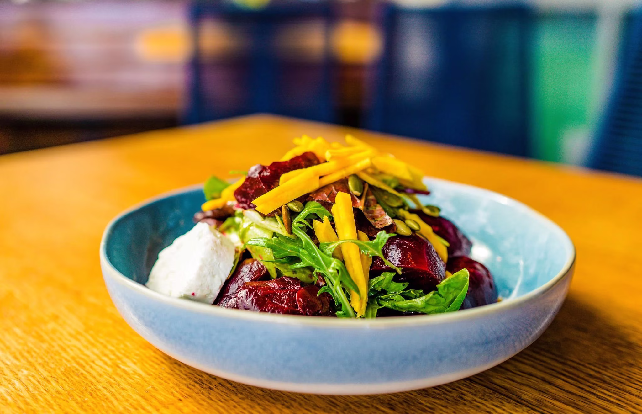 A colorful salad of beets, greens, mango, and cheese in a blue bowl.