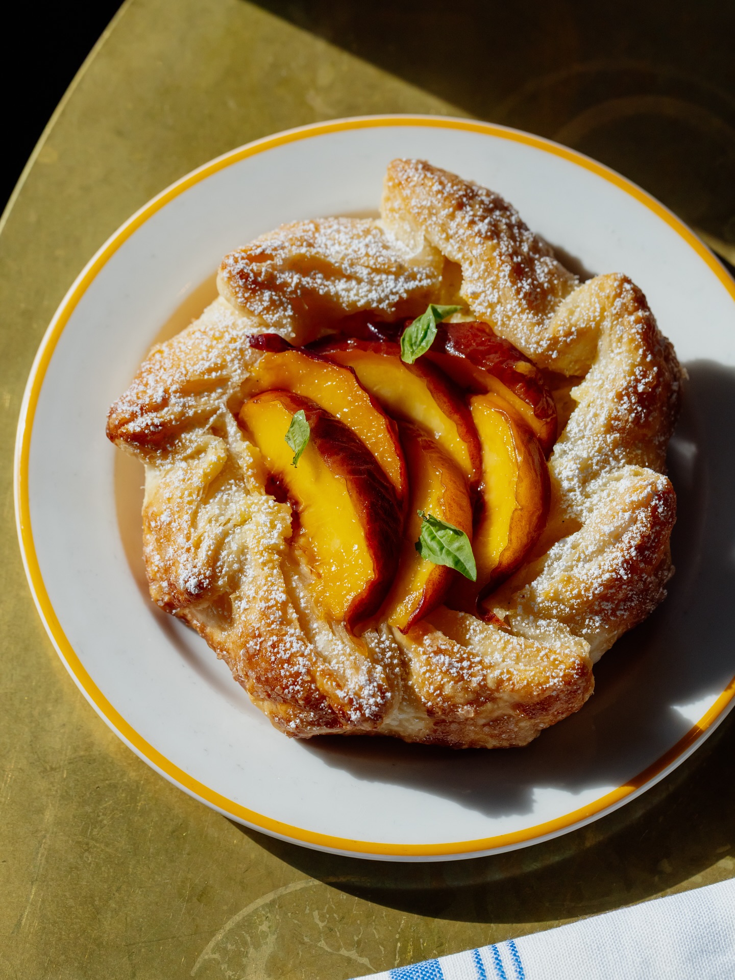 Peach galette with powdered sugar and green leaves on a white plate.
