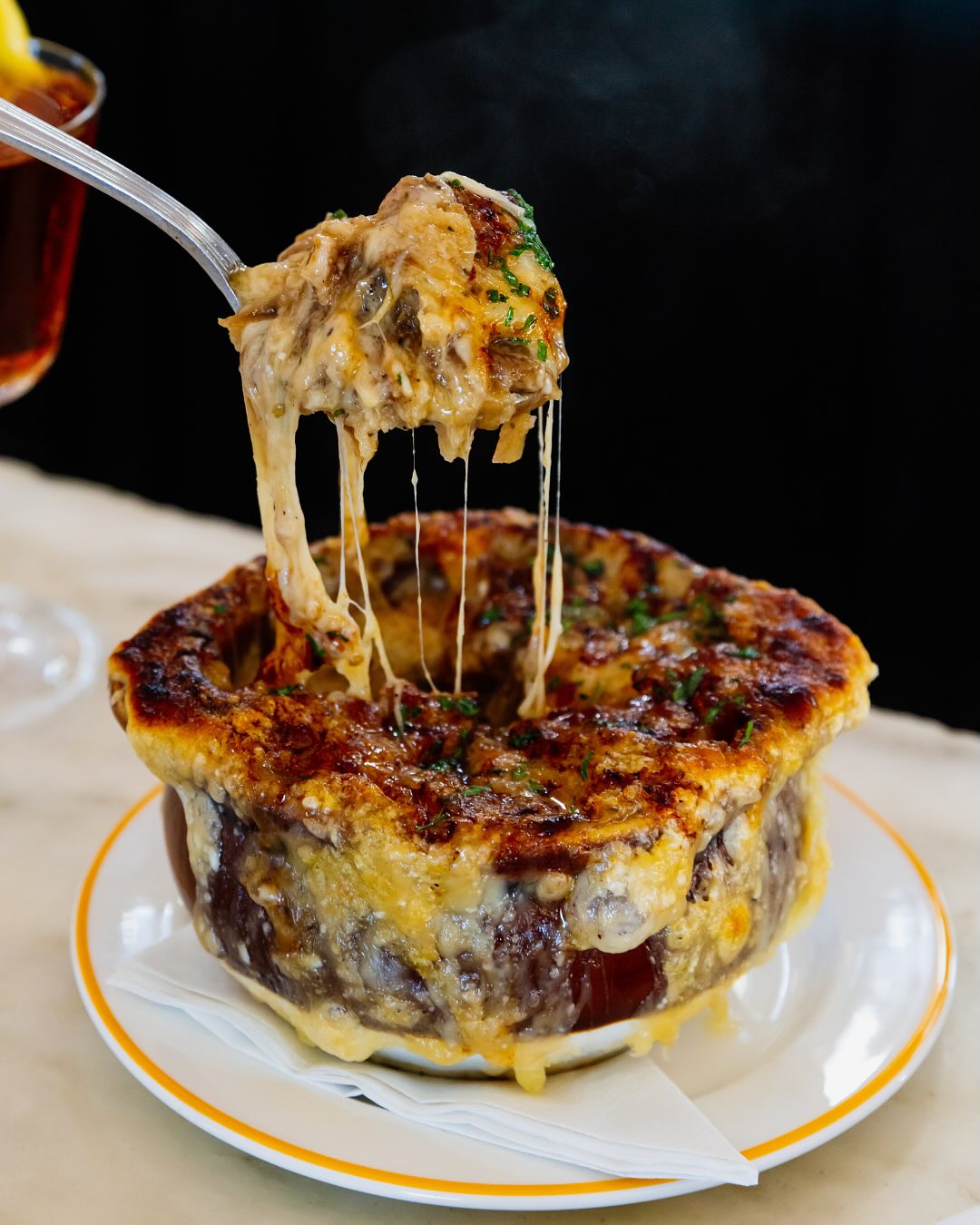 Spoon lifting cheesy French onion soup from a bowl with cheese pull.