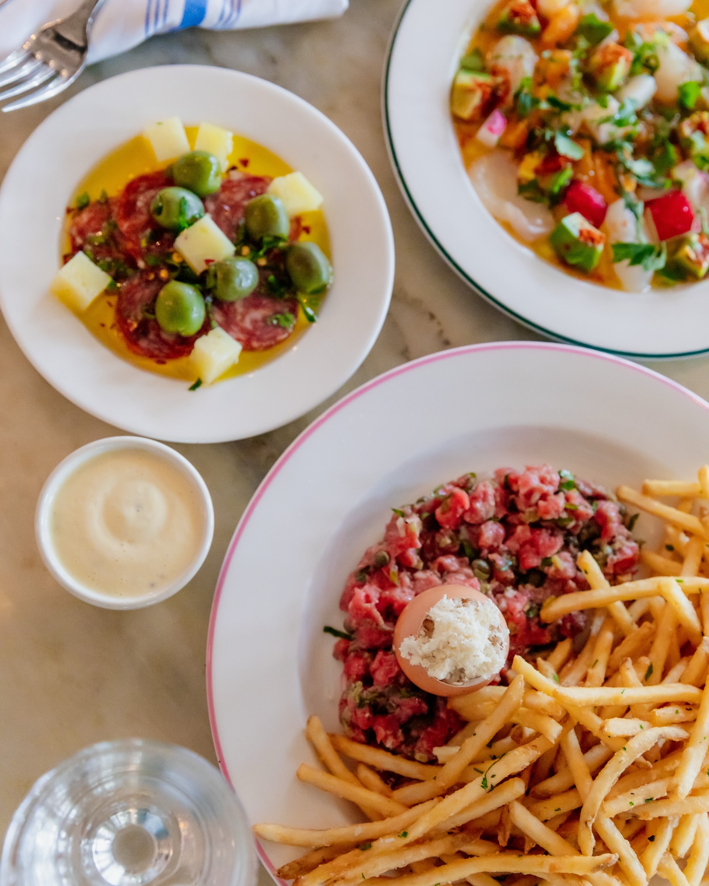 Steak tartare with fries, salami, olives, and ceviche on plates.