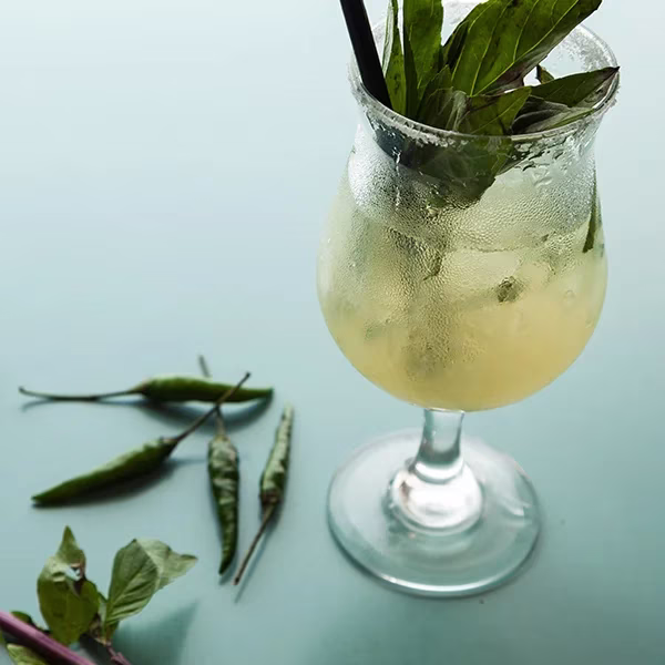 A basil and chili cocktail with peppers on a blue surface.