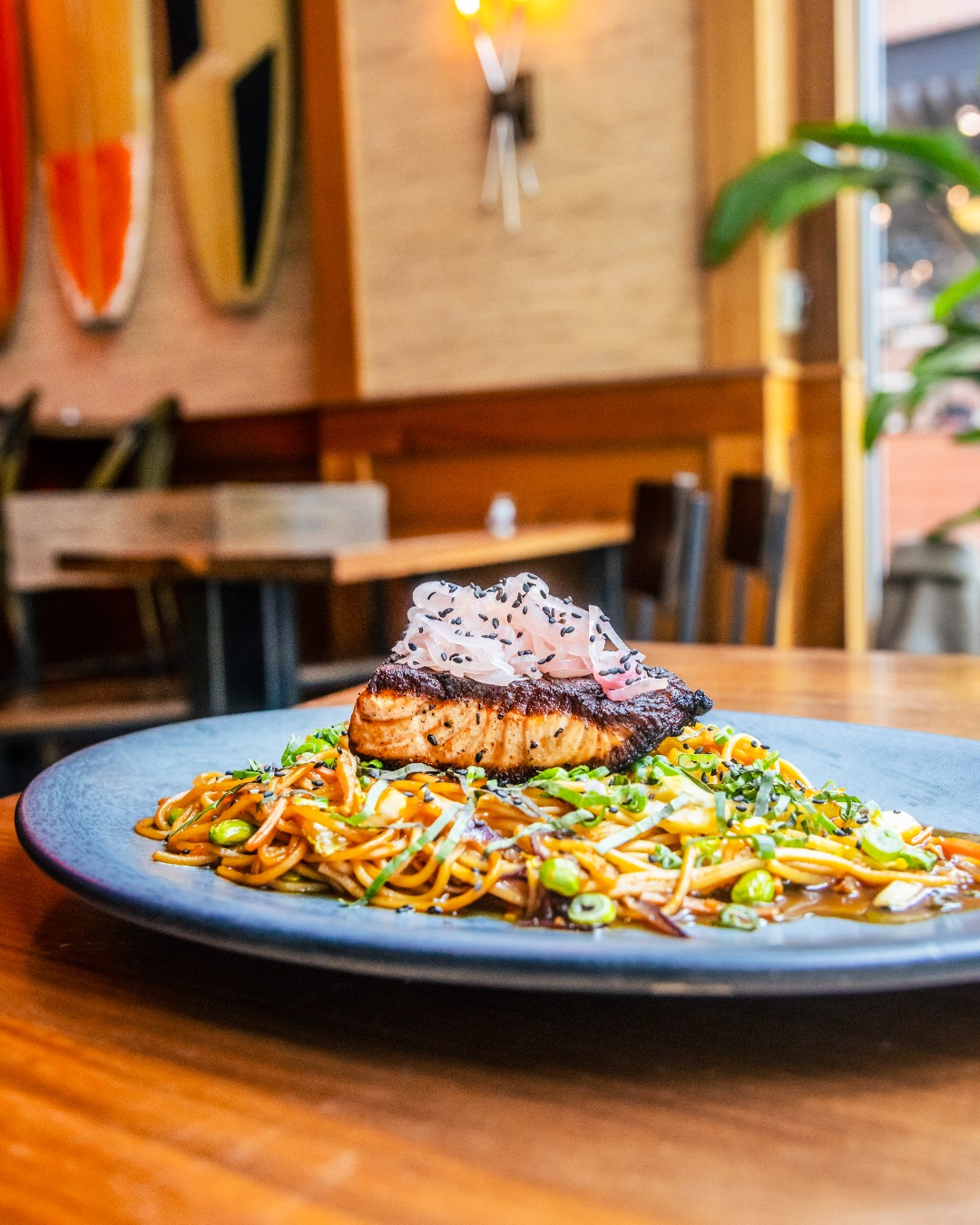 Seared fish on noodles, topped with pickled onions and sesame seeds.