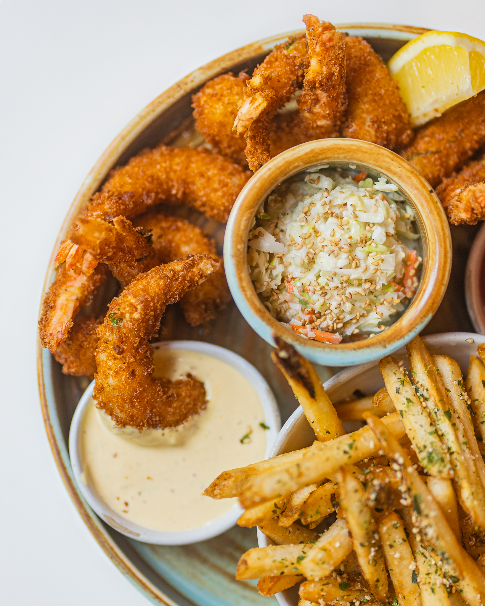 Fried shrimp, coleslaw, french fries, lemon, and dipping sauces on a platter.