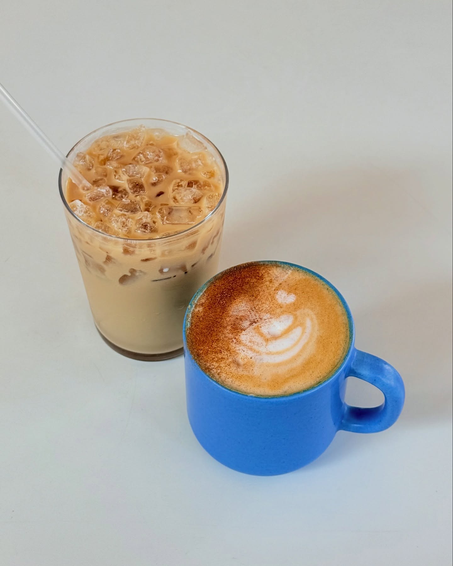 Iced coffee in glass and a latte with art in blue mug.