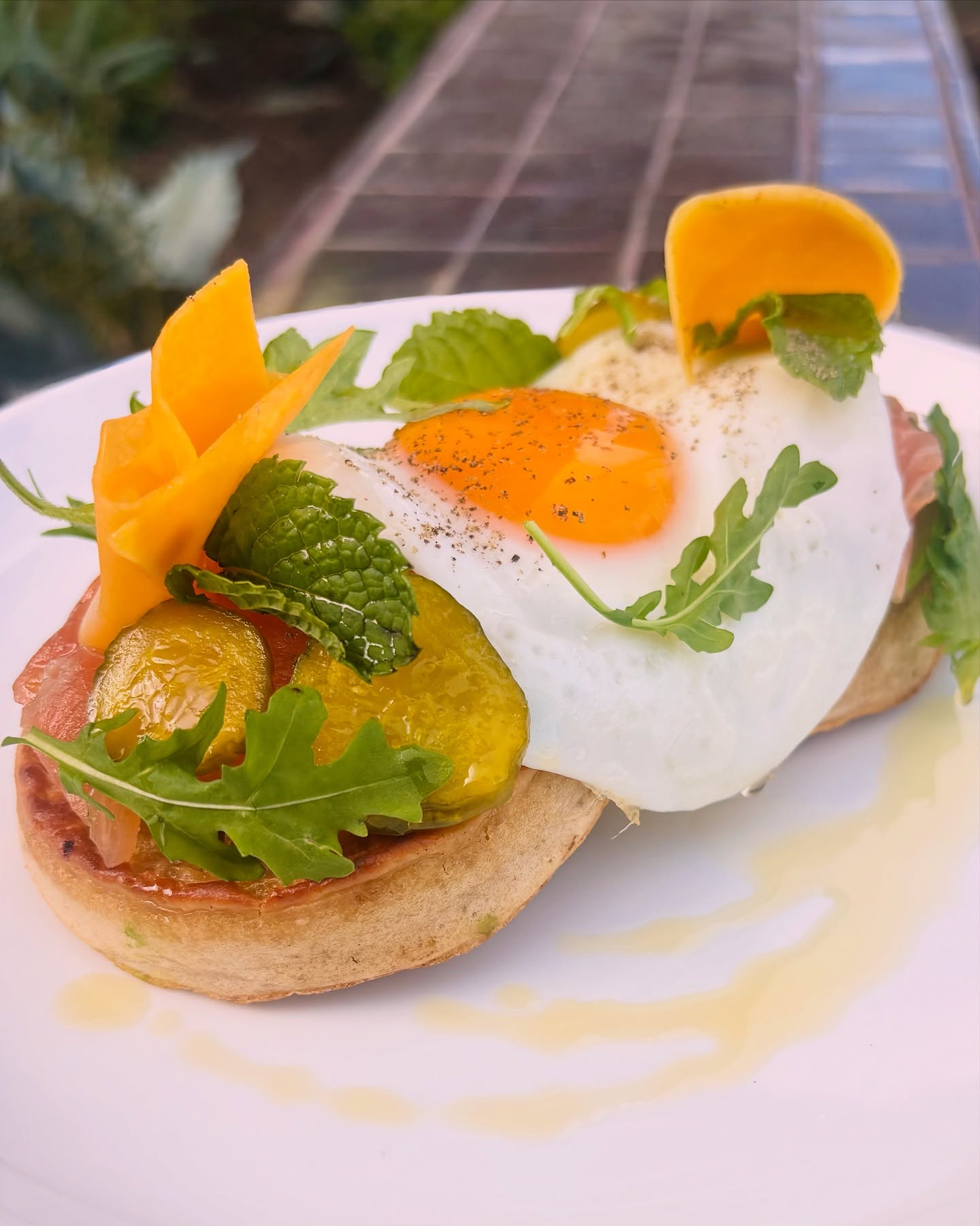 Fried egg, carved fruit, pickles, ham, and greens on a thick muffin.