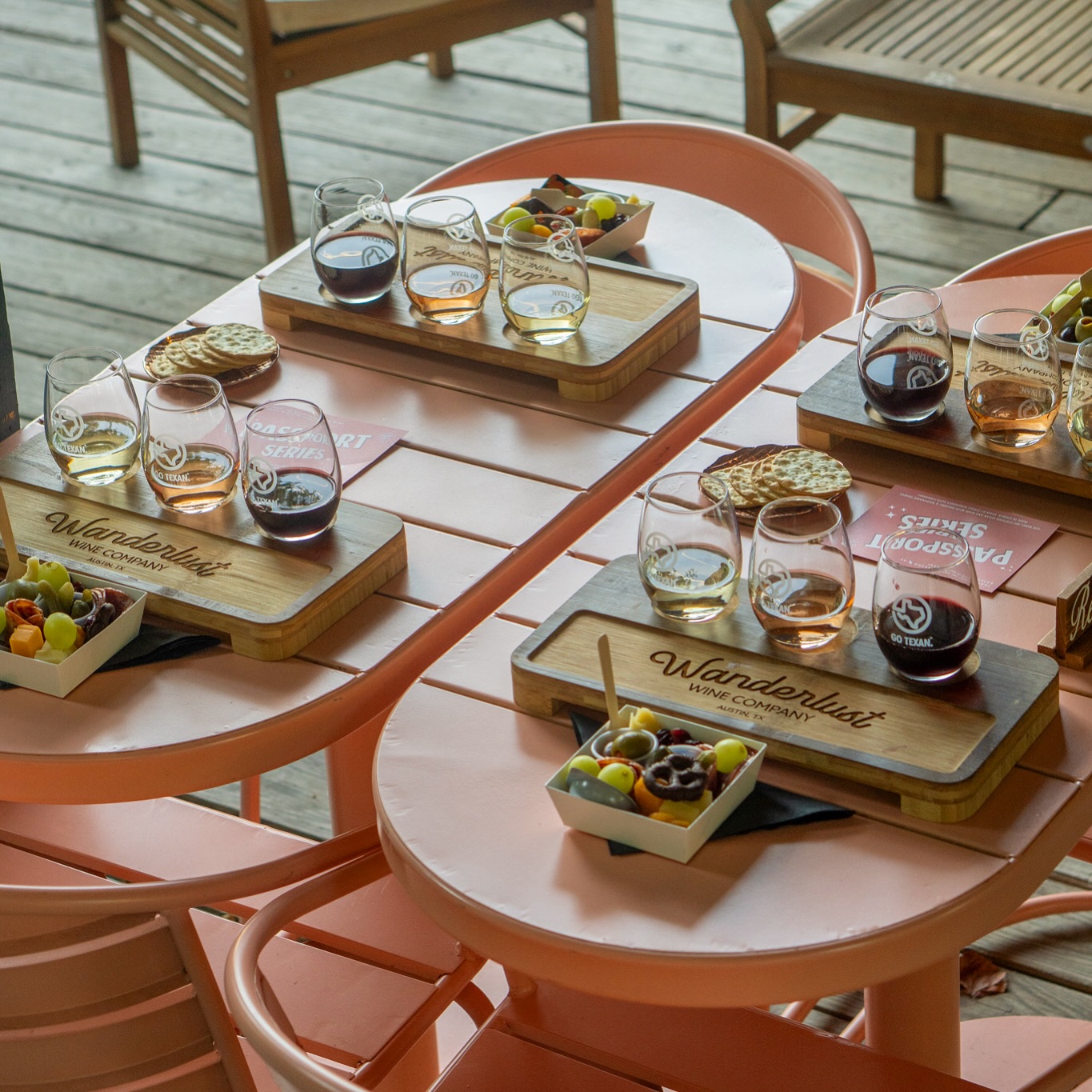 Wine tasting flights with snacks on peach-colored outdoor tables.