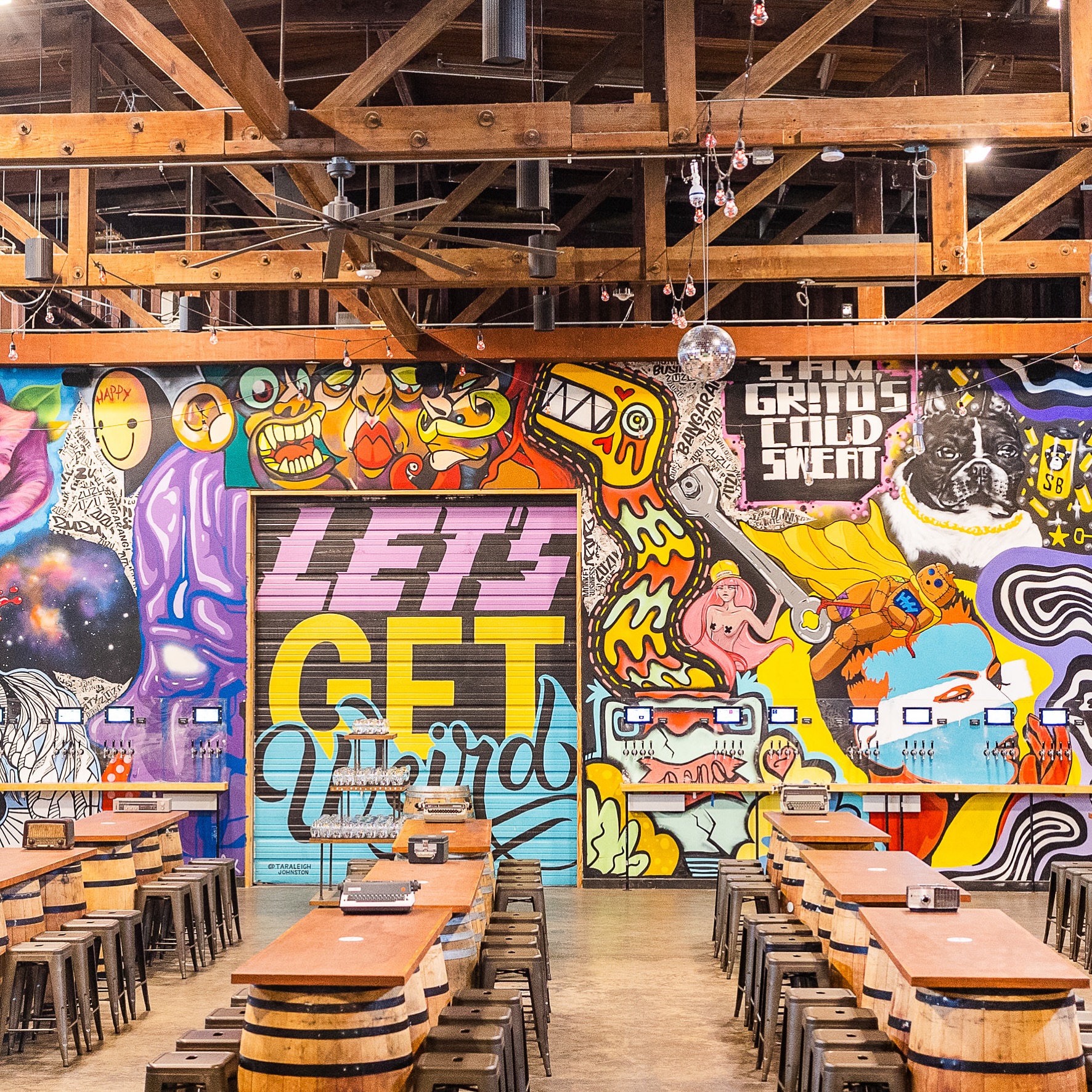 Vibrant room with graffiti art, barrel tables, stools, and beverage taps.
