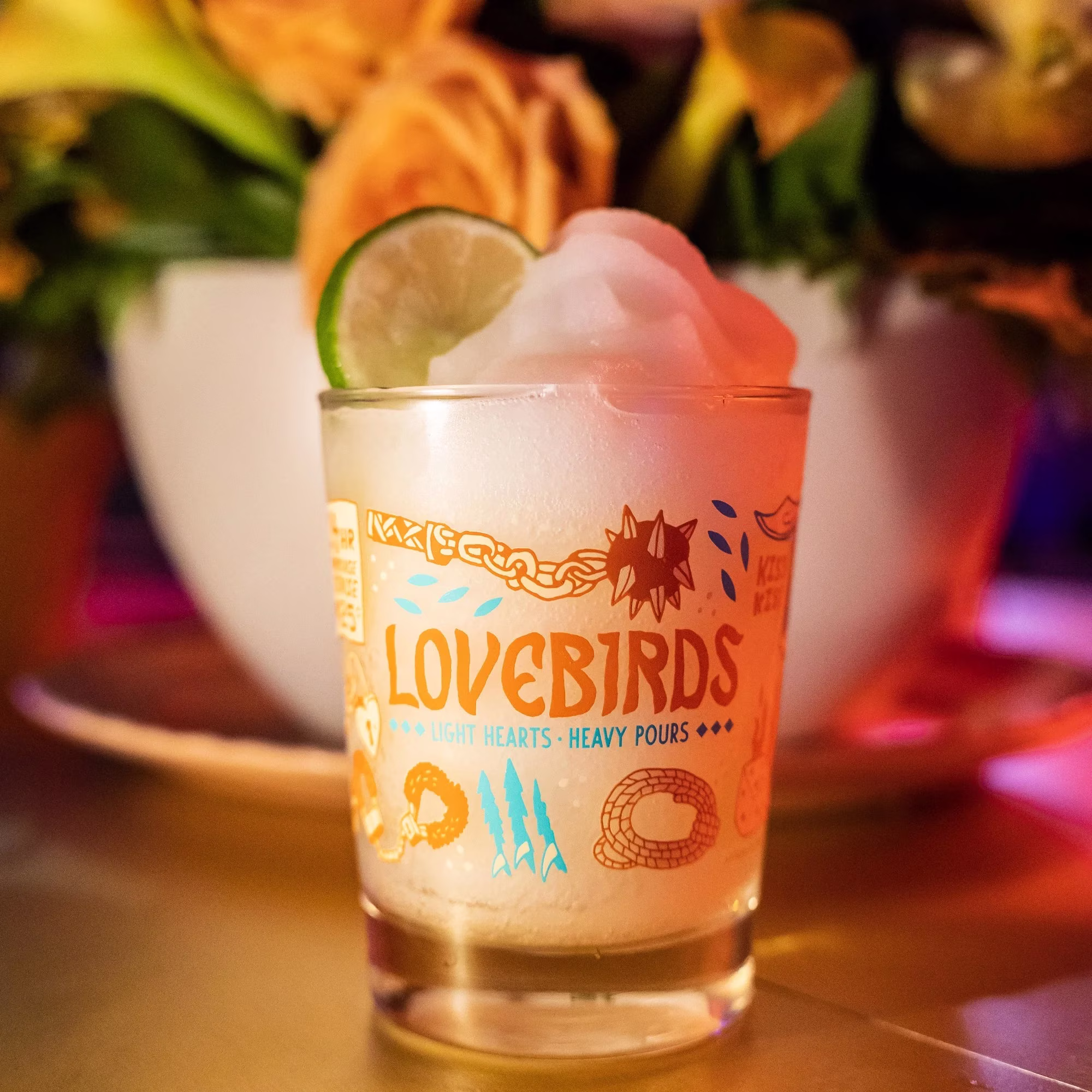 A Lovebirds branded glass with a drink, lime, and white topping.