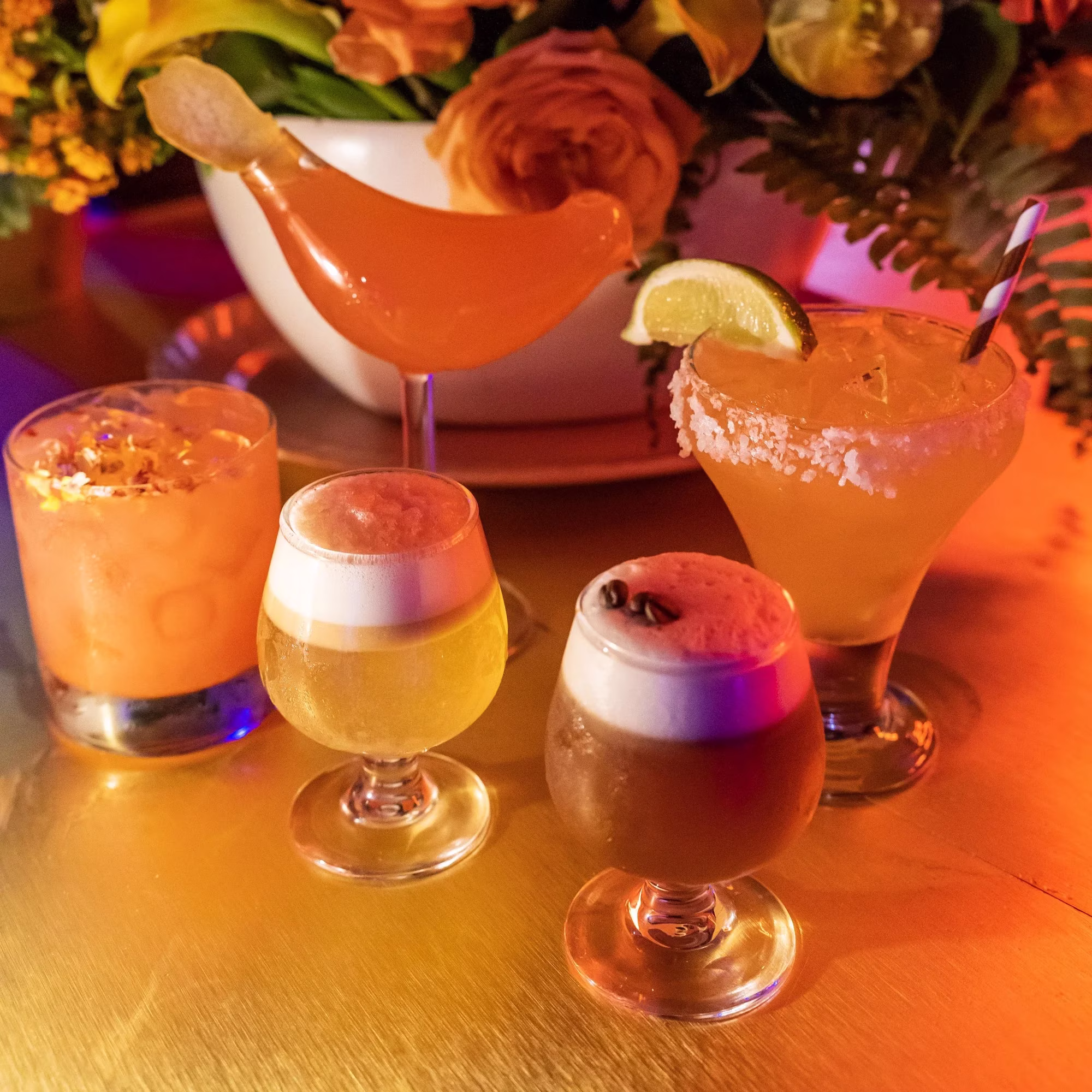 Four different cocktails and beverages on a warm-lit table.