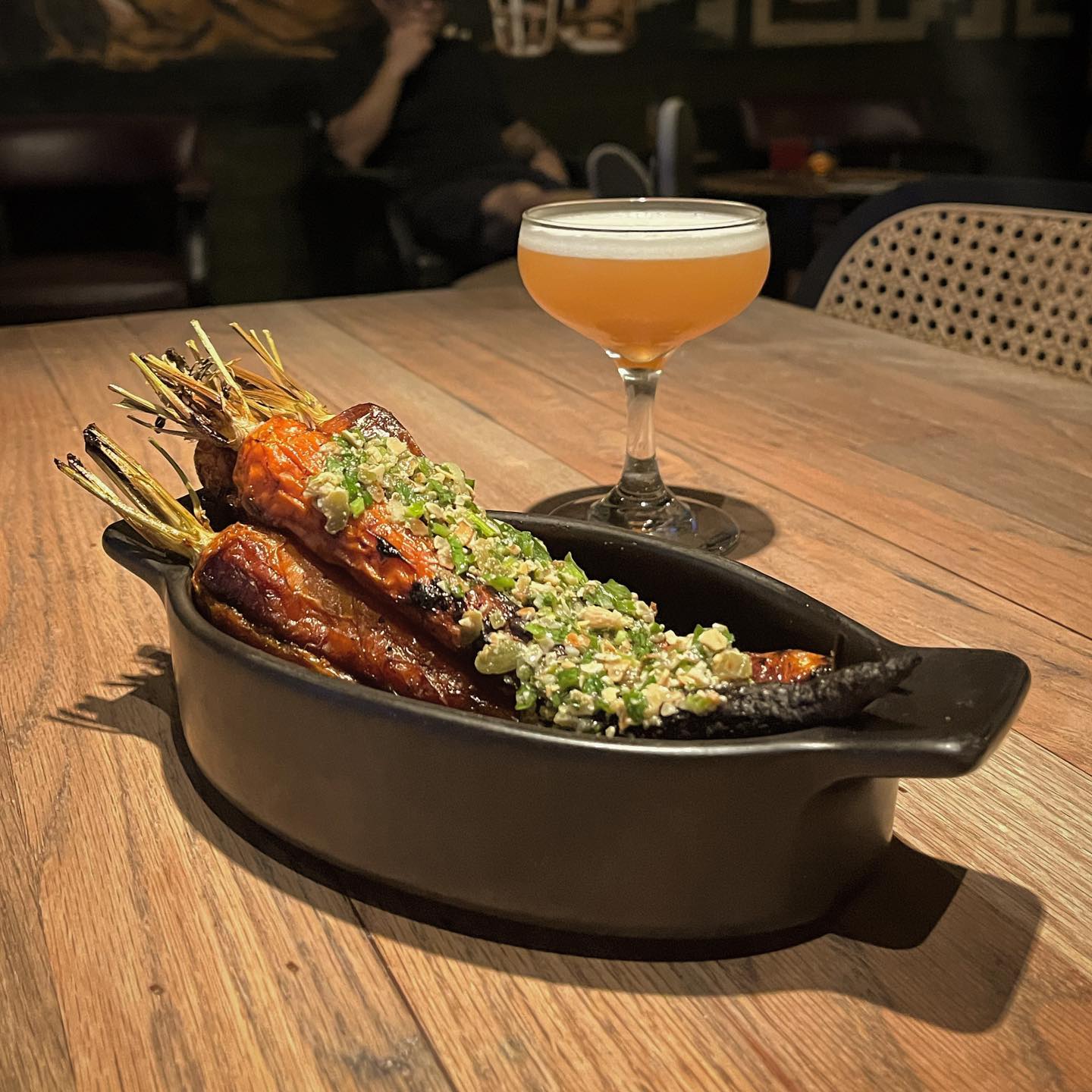 Roasted carrots topped with relish and a cocktail in a coupe glass.