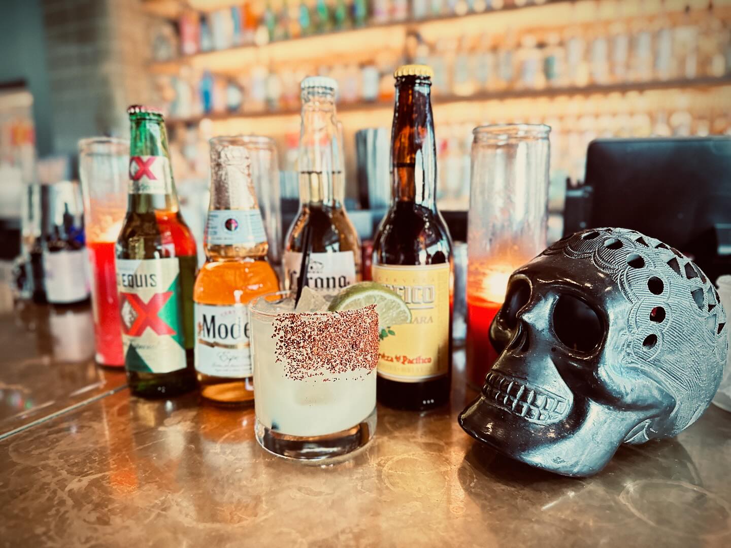 Beer bottles, margarita, and skull decoration on a bar counter.