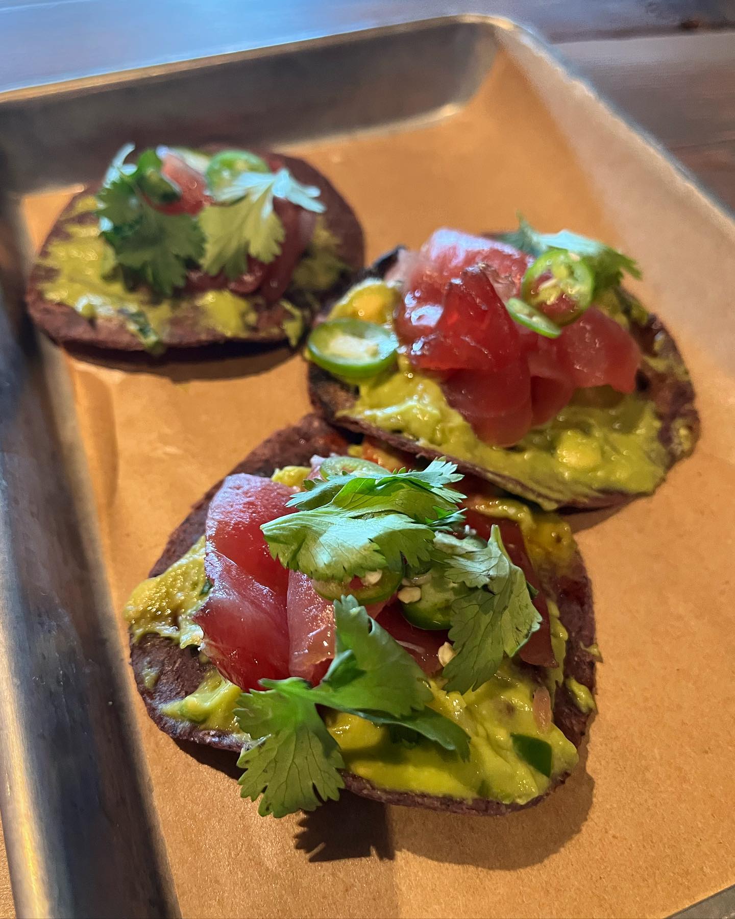 Three tuna tostadas with guacamole, jalapeños, and cilantro on a tray.