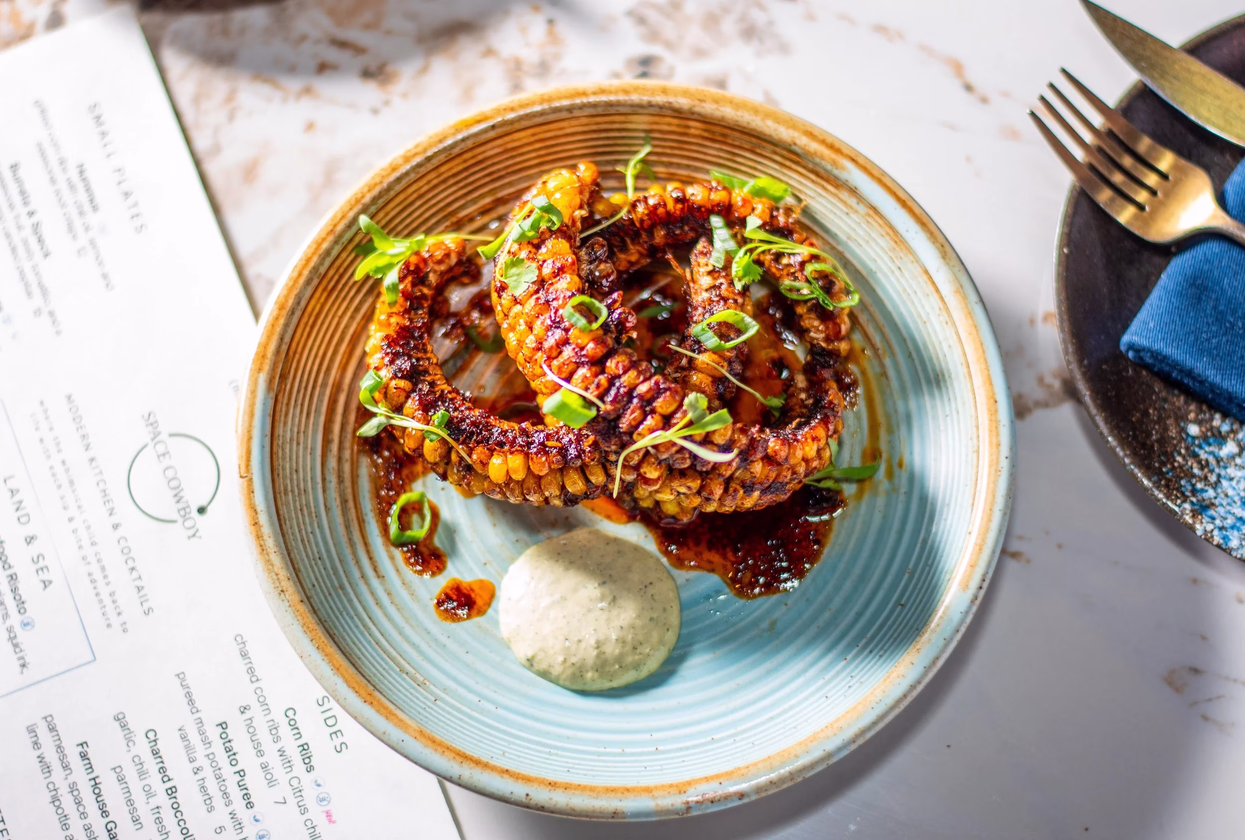 Charred corn ribs with sauces and herbs on a blue plate.