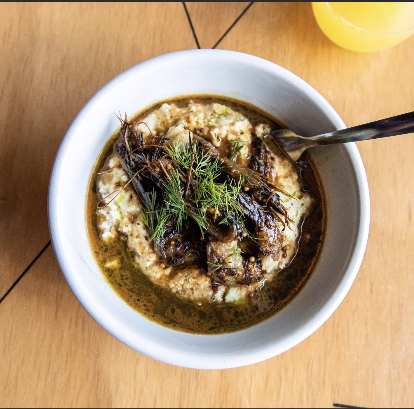 Bowl of grits with head-on dark prawns and green herbs.