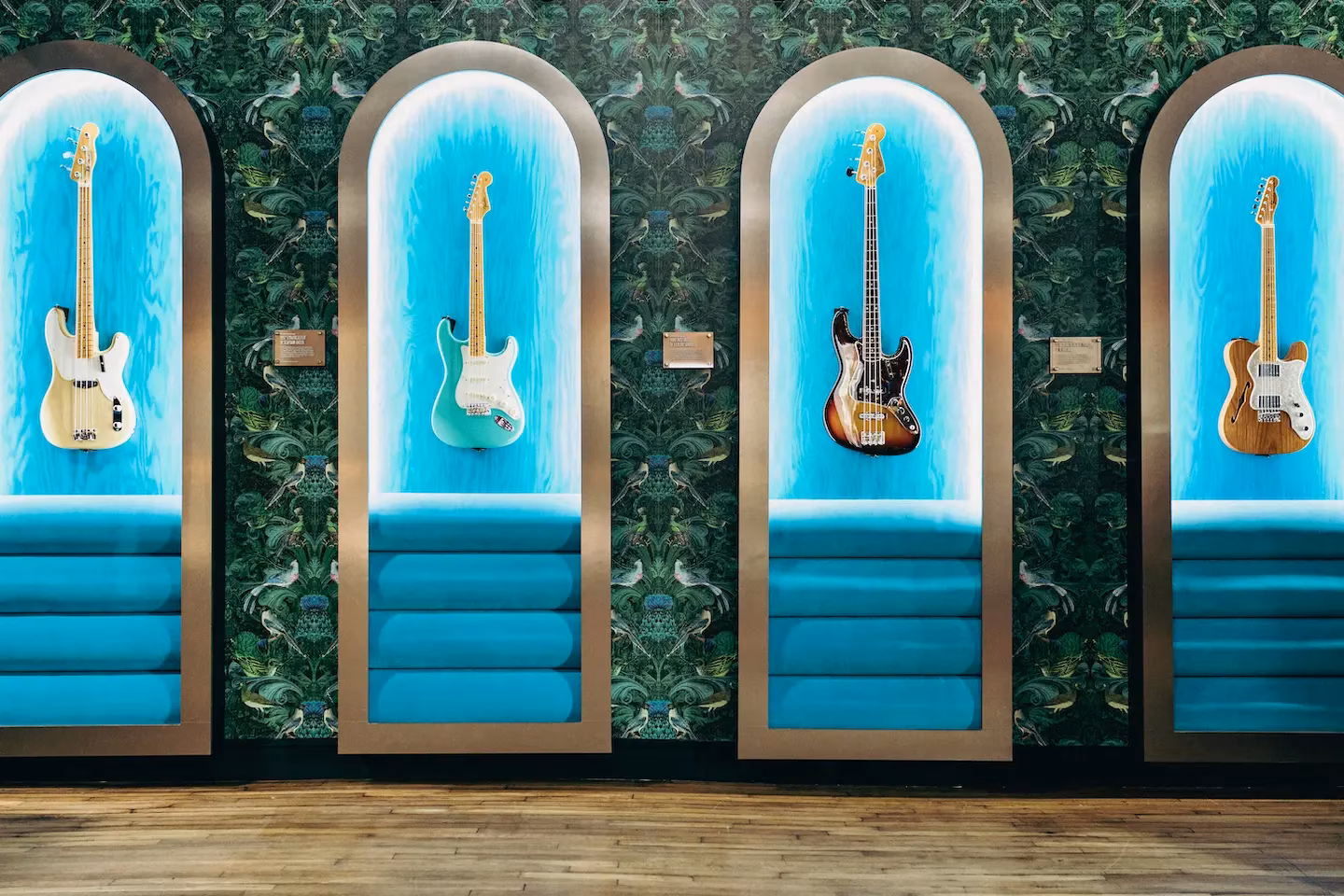 Four electric guitars in arched displays against green patterned wallpaper.
