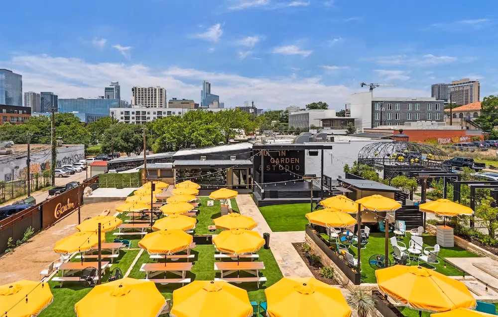 Outdoor In Garden & Studio venue with yellow umbrellas and cityscape.