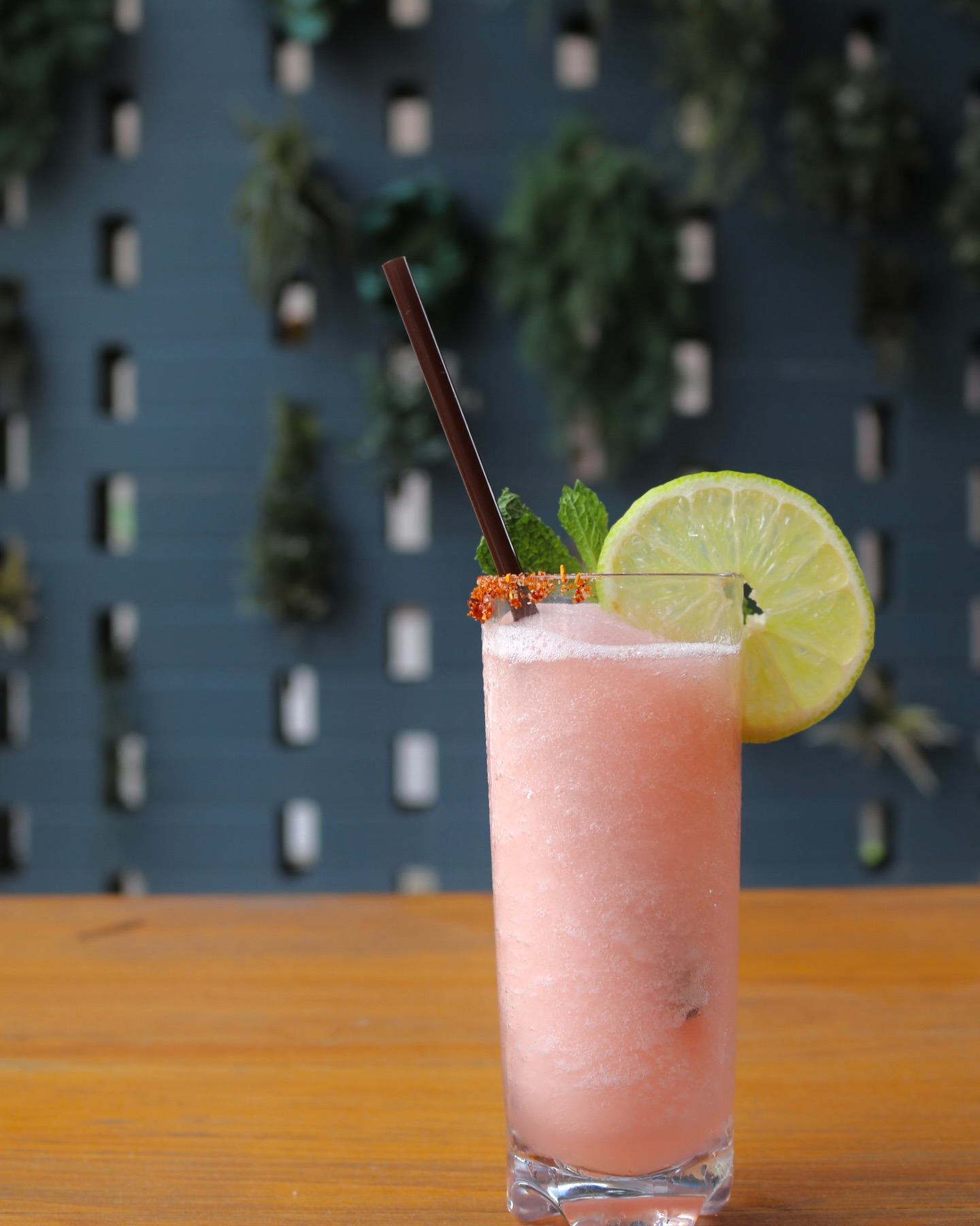 Pink frozen drink with lime, mint, straw, and red-orange rim.