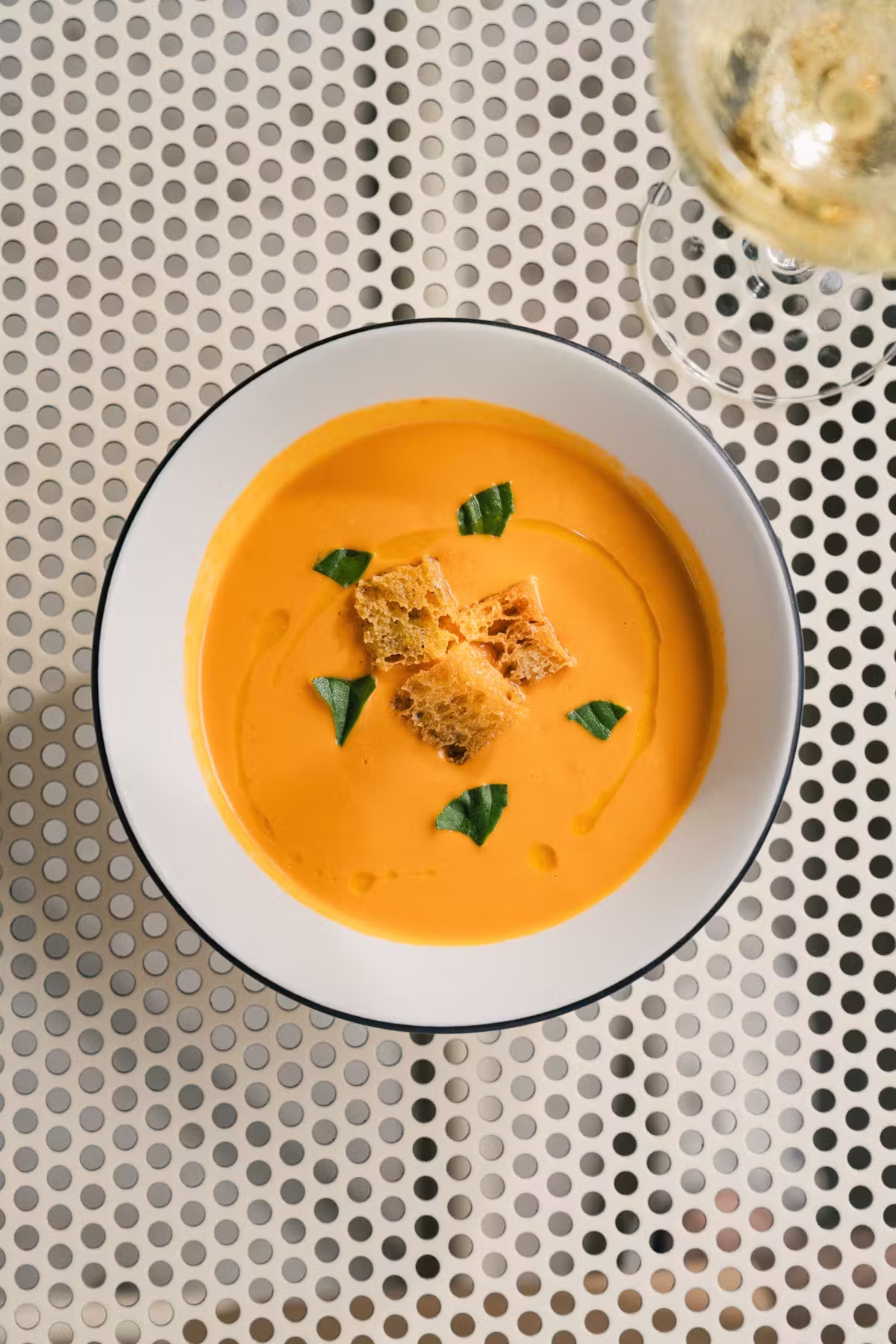Orange soup, croutons, green leaves, wine glass, perforated table.