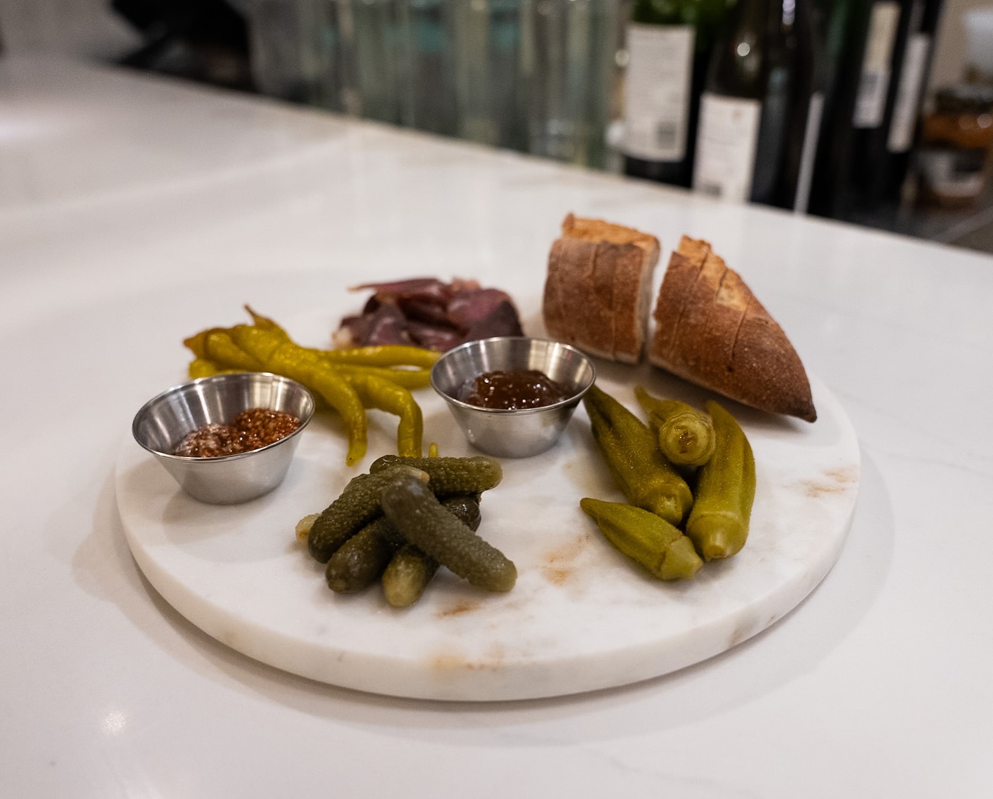 Marble board with sliced bread, cured meat, pickled vegetables, and sauces.