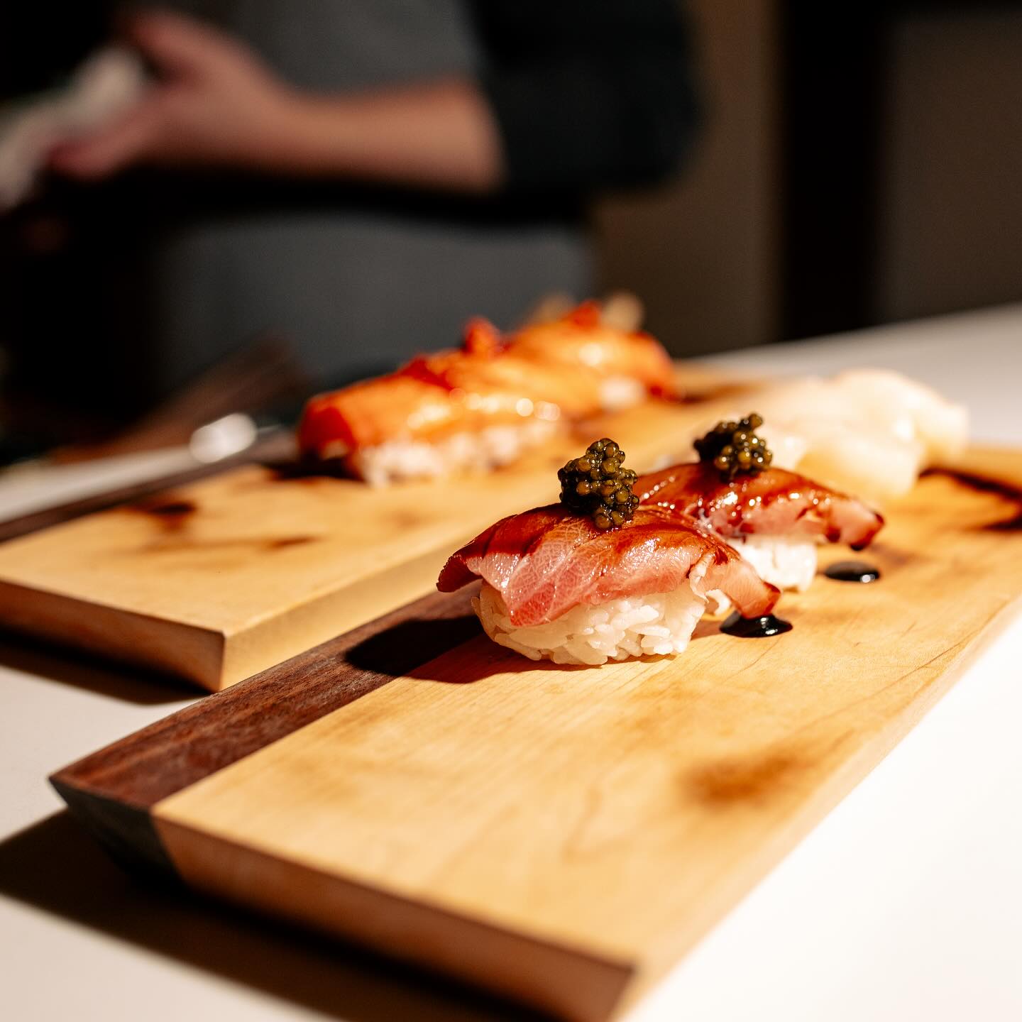 Nigiri sushi with caviar and sauce on two wooden boards.