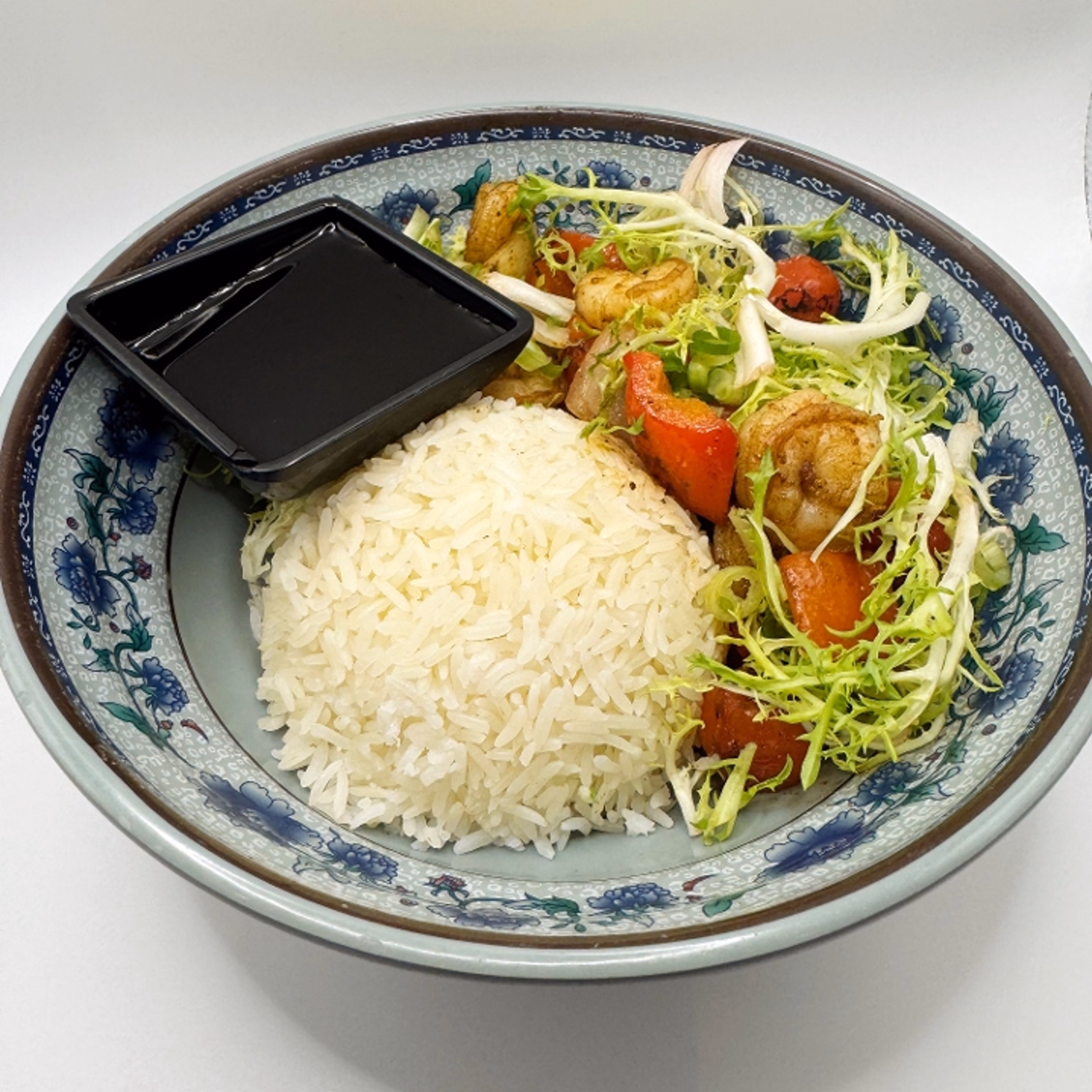 Bowl of rice, shrimp, salad, and sauce in a patterned bowl.