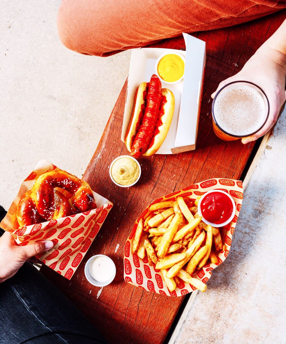 Hot dog, pretzel, fries, and beer on a wooden table.