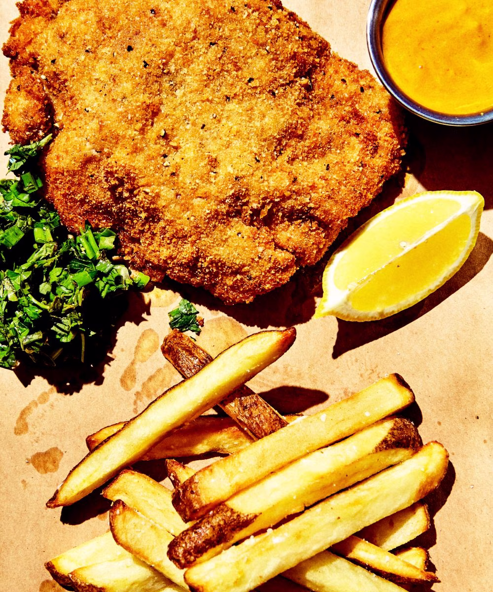 Breaded fried cutlet, french fries, lemon, sauce, and greens.