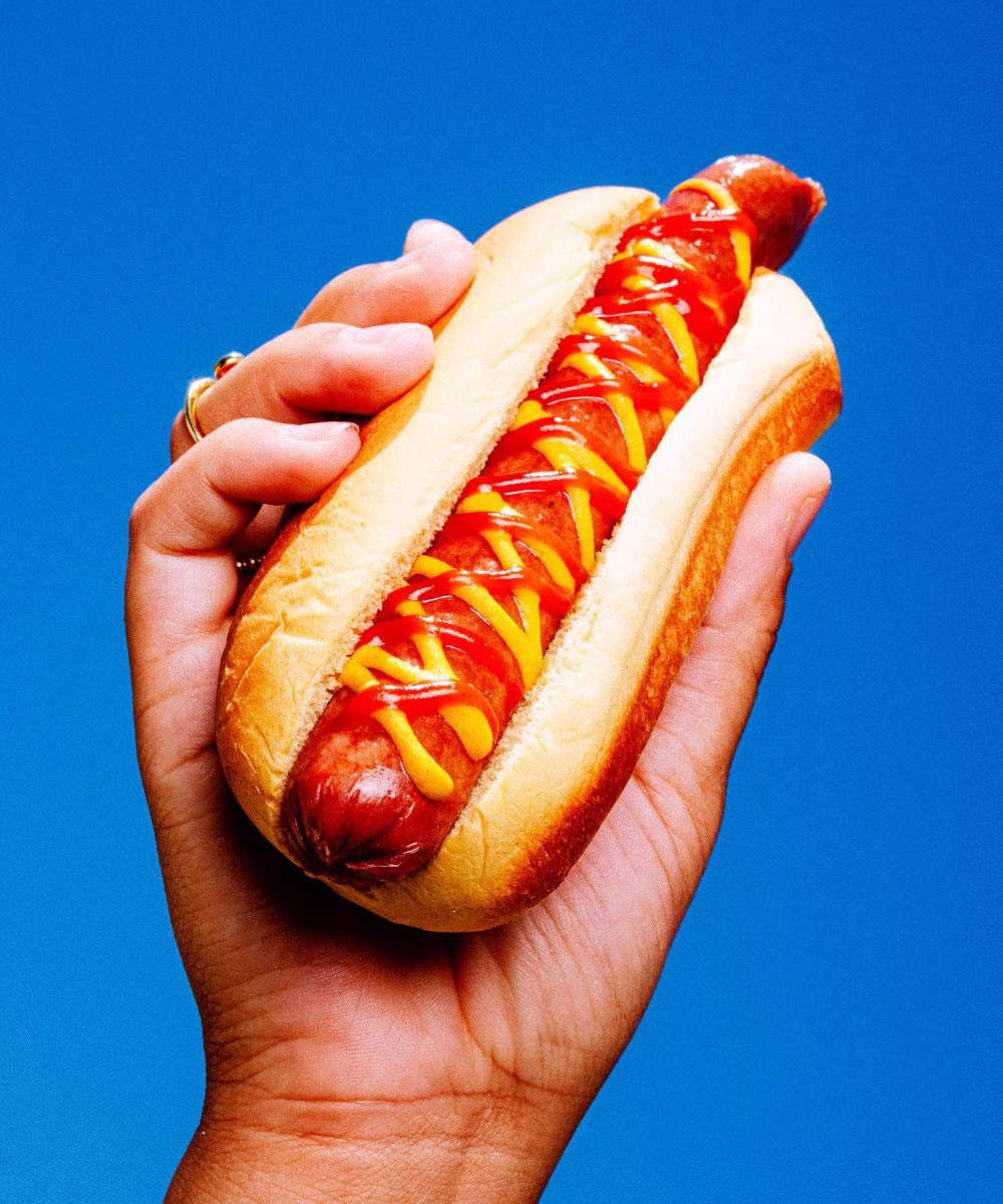 A hand holds a hot dog with ketchup and mustard.