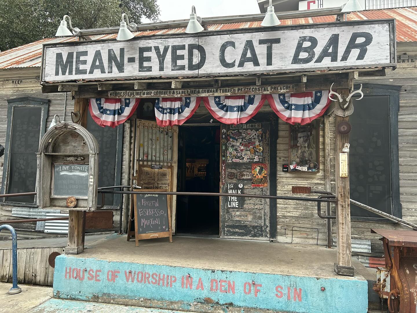 Mean-Eyed Cat Bar exterior with patriotic buntings and a chalkboard.