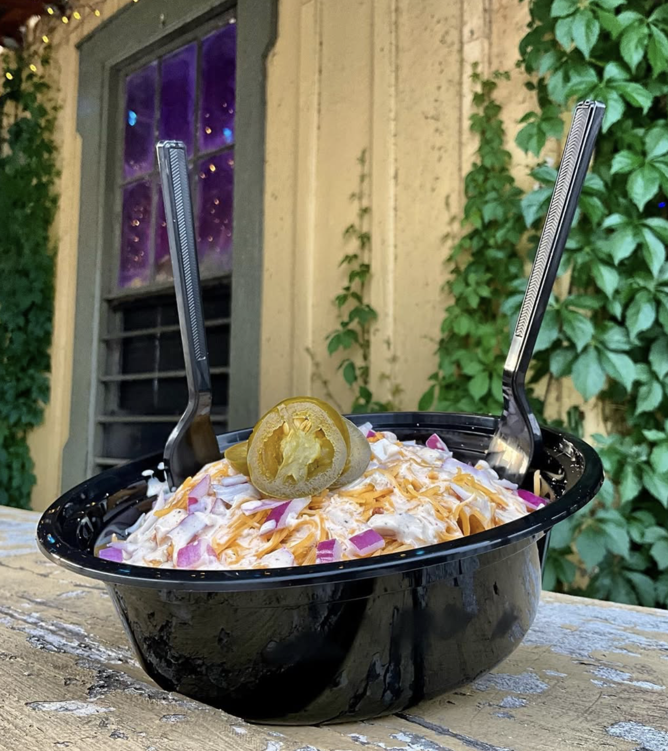 Black bowl of creamy food with cheese, red onion, jalapeños, and forks.