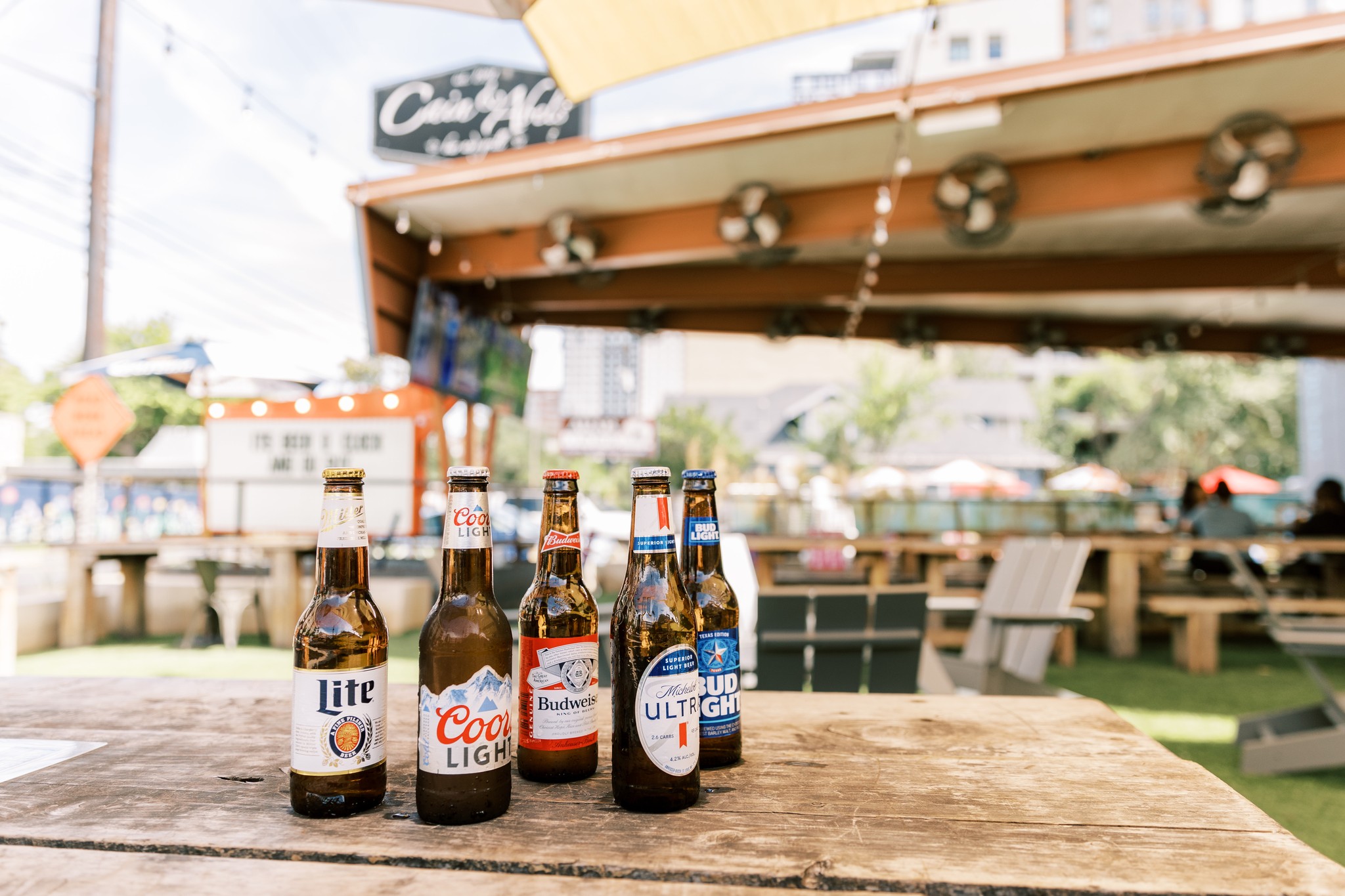 Five beer bottles sit on an outdoor table at a beer garden.
